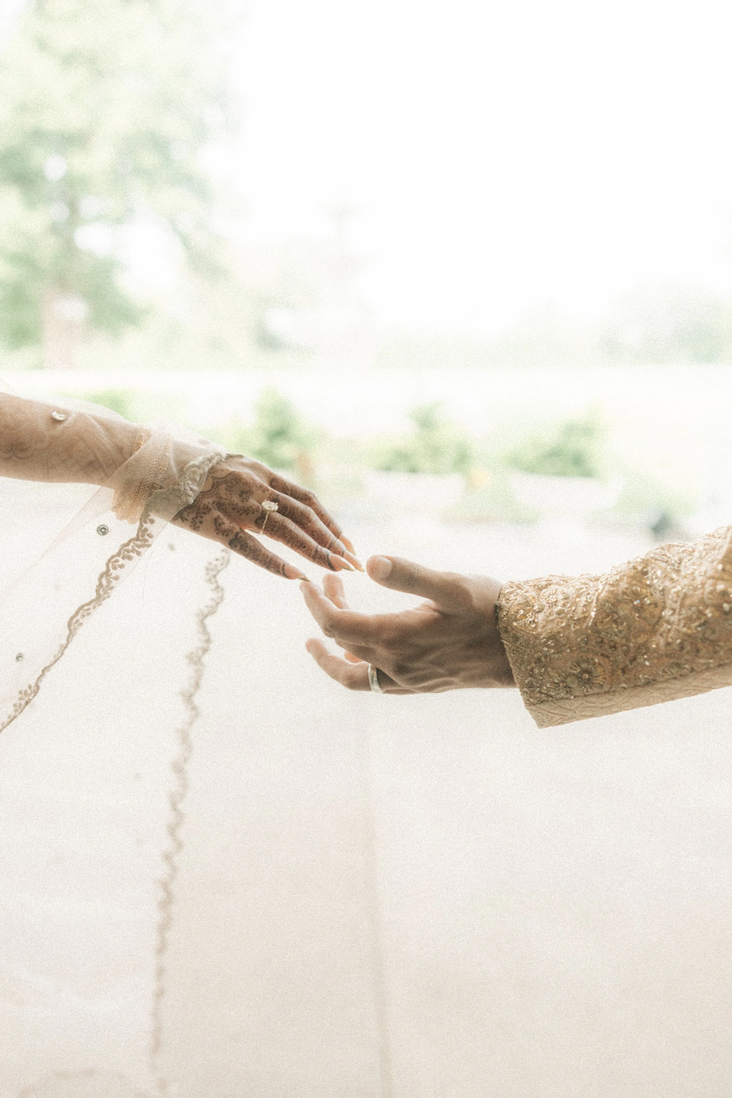 Close-up of two hands reaching out to each other, one hand in ornate traditional attire and the other in a simple long-sleeved garment, against a bright and soft background.