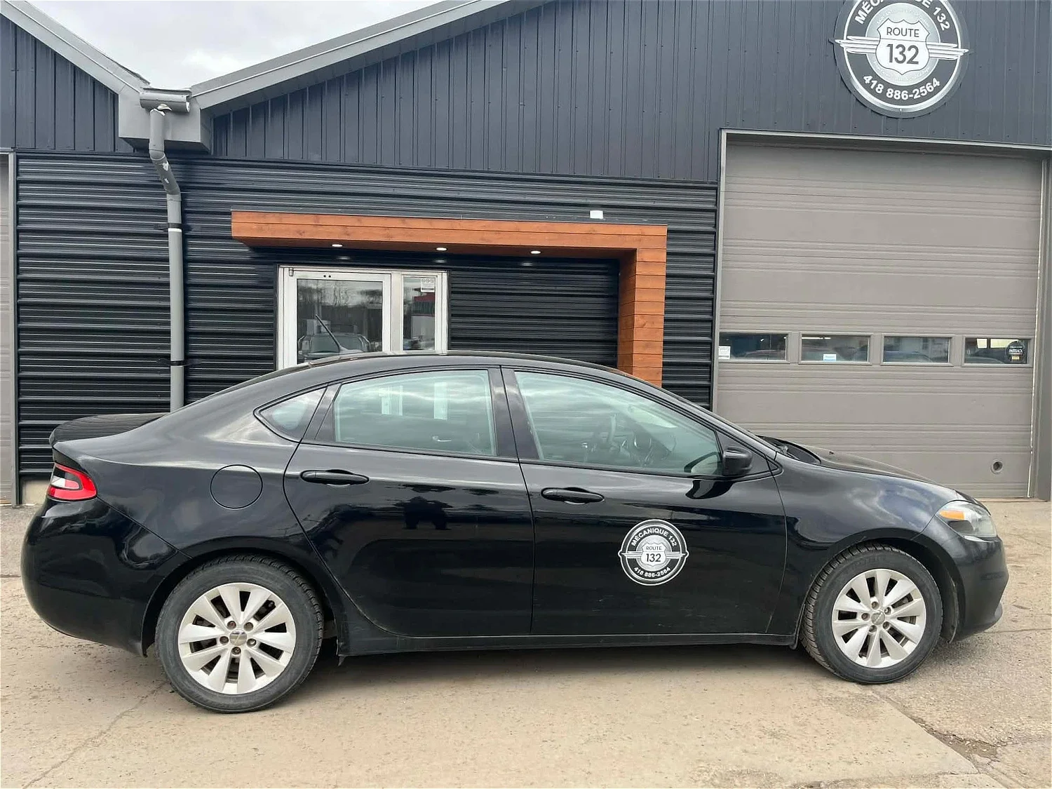 Voiture noire stationnée devant un bâtiment, logo de l'entreprise Mécanique 132 affiché sur la porte et la voiture.