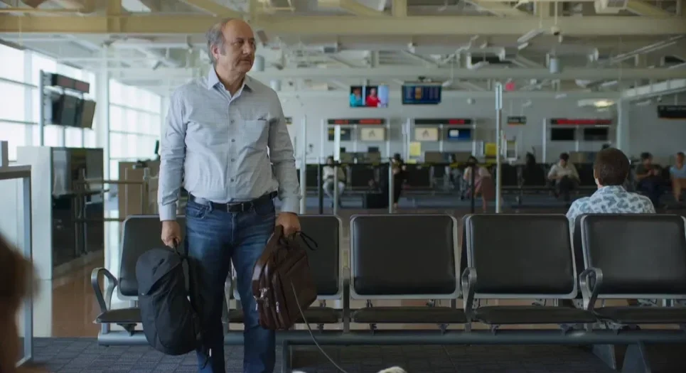 A man walking through an airport terminal carrying a backpack and a briefcase.