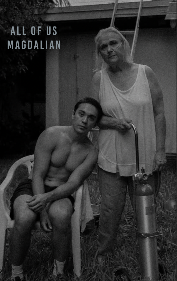 A black and white photo of a shirtless young man sitting on a plastic chair next to an elderly woman standing beside him under a wooden structure. The woman is using a portable oxygen tank and a nasal oxygen tube. Text in the upper left corner reads 