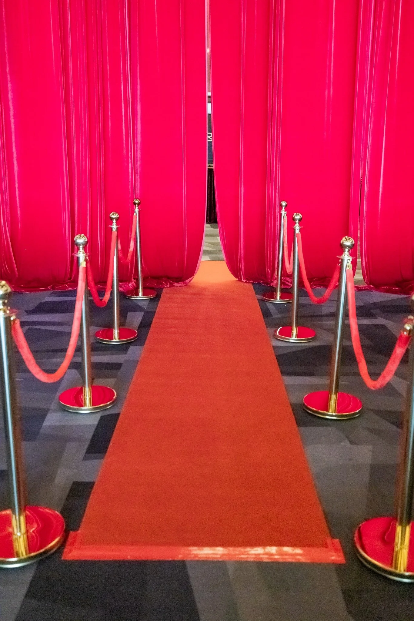 Red carpet leading through pink velvet curtains, with gold stanchions and red ropes on either side.