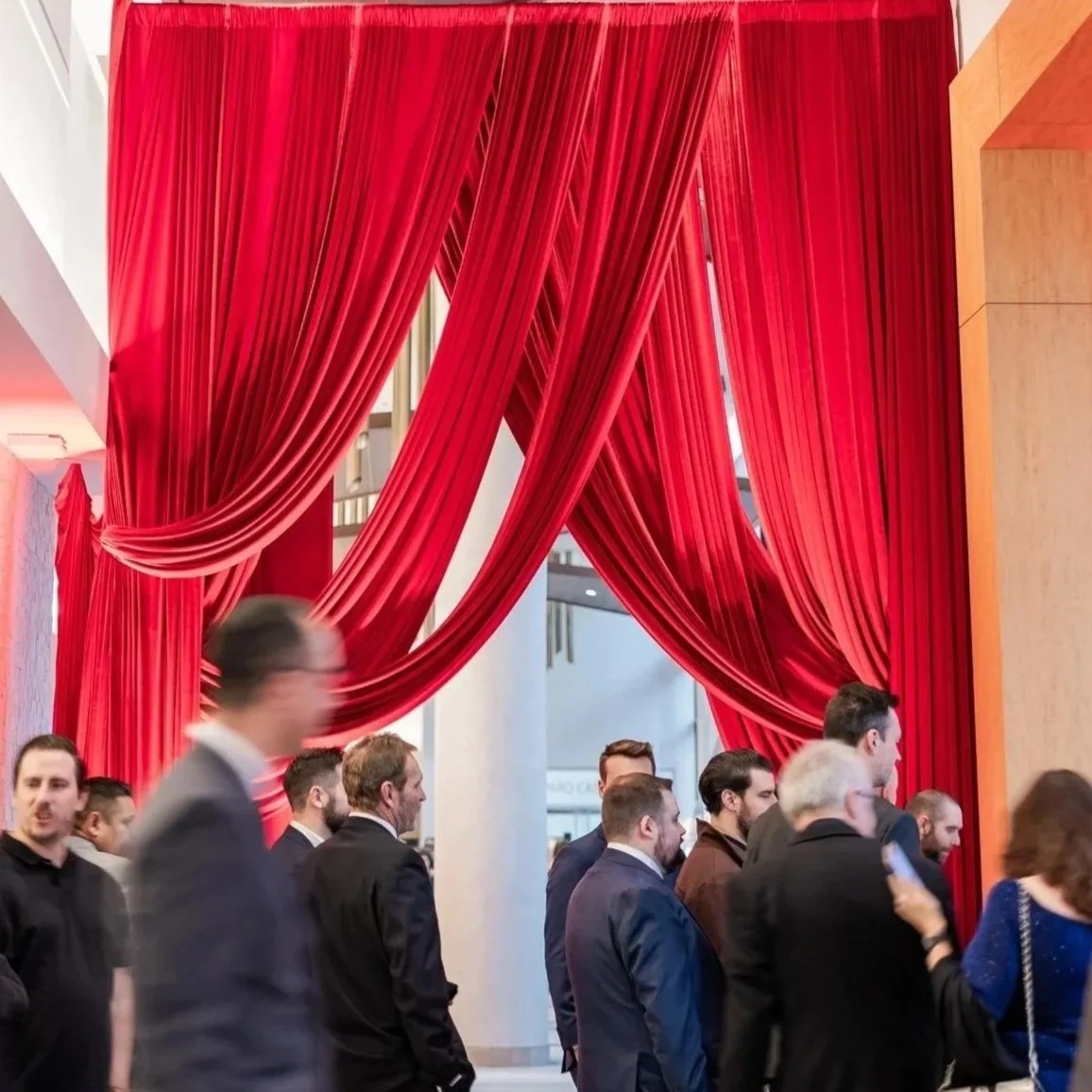 Group of people walking past large red velvet curtains at an event or venue.