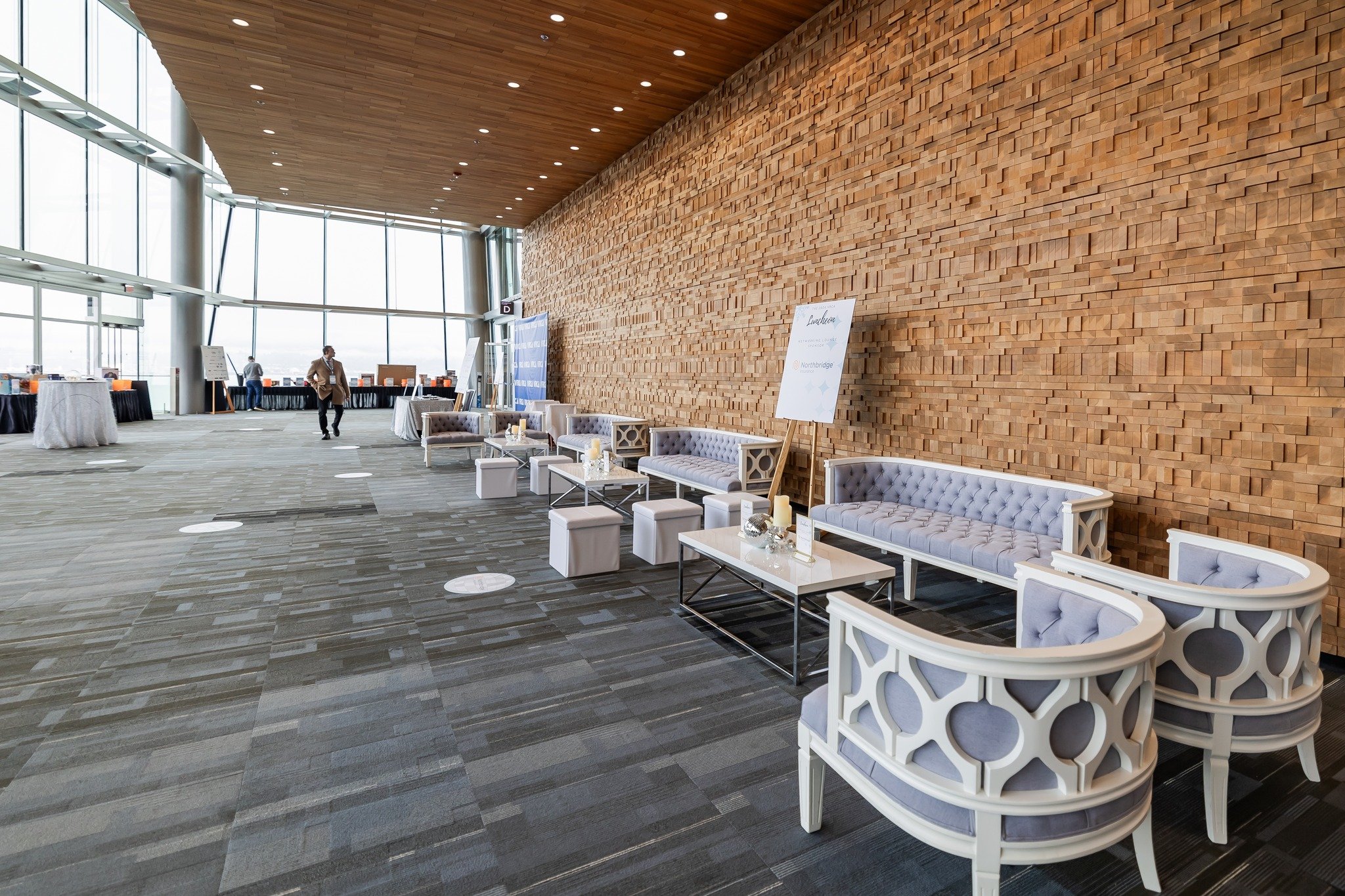 Modern banquet or conference room with a large wooden accent wall, glass windows, and white and lavender seating arrangements.