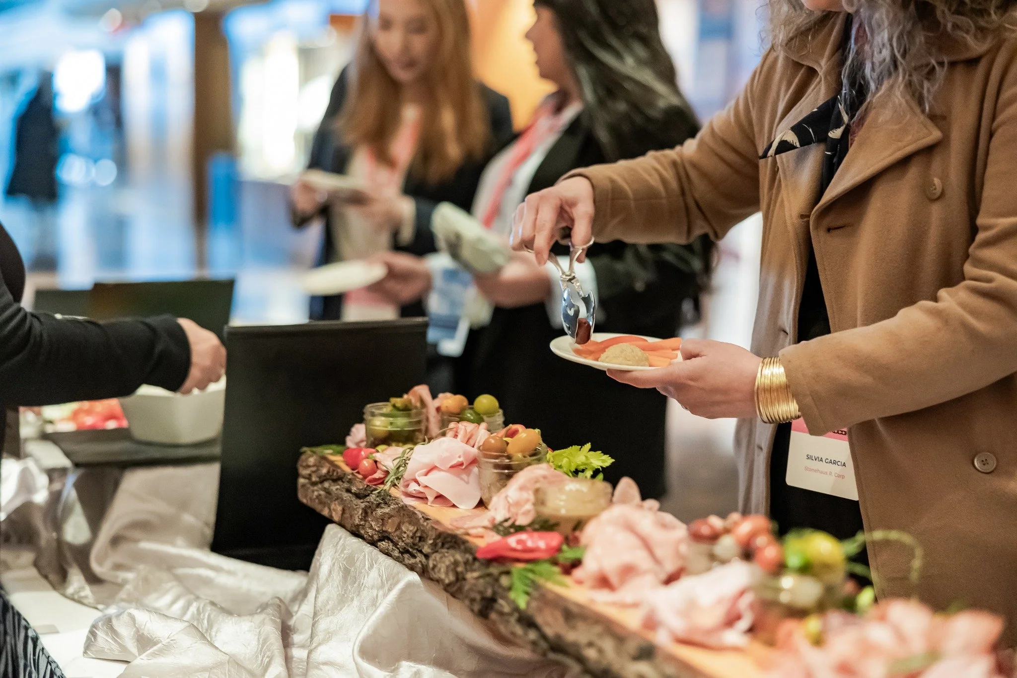 People serving themselves food from a buffet table with various appetizers and snacks on a wooden board at a social event.
