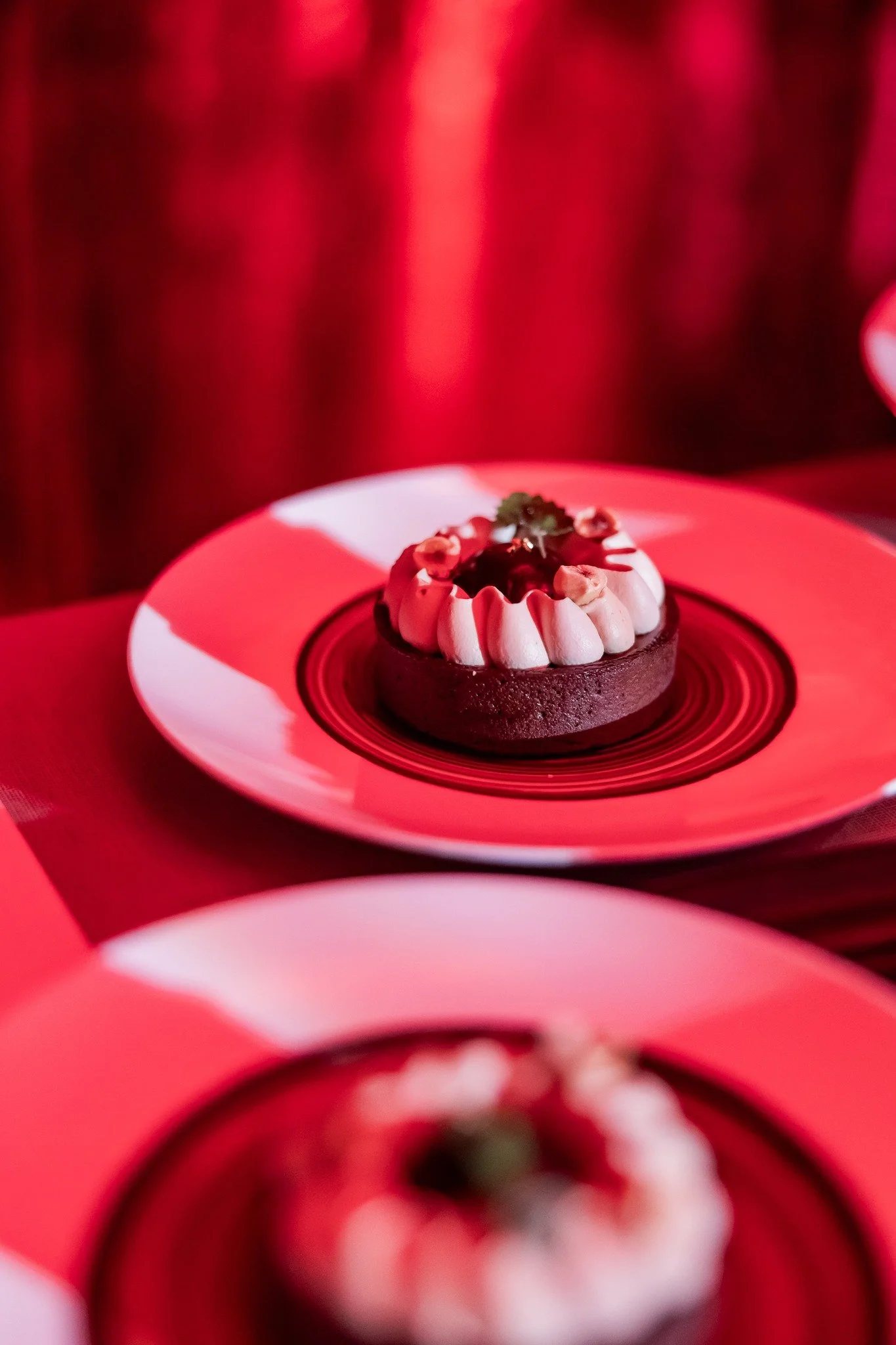 A chocolate dessert with white piping, garnished with a sprig of mint and nuts, served on a striped black and white plate.