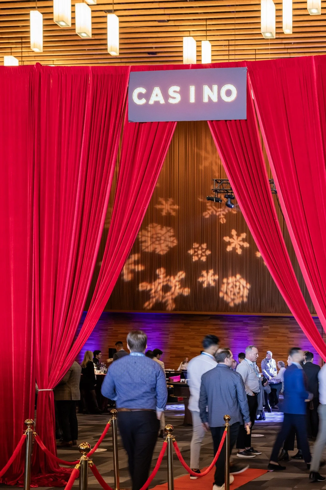 Entrance to a casino with red curtains and a sign that says 'CASINO.' People are walking inside the venue, which has a decorated wall with snowflake-shaped lights projected onto it.
