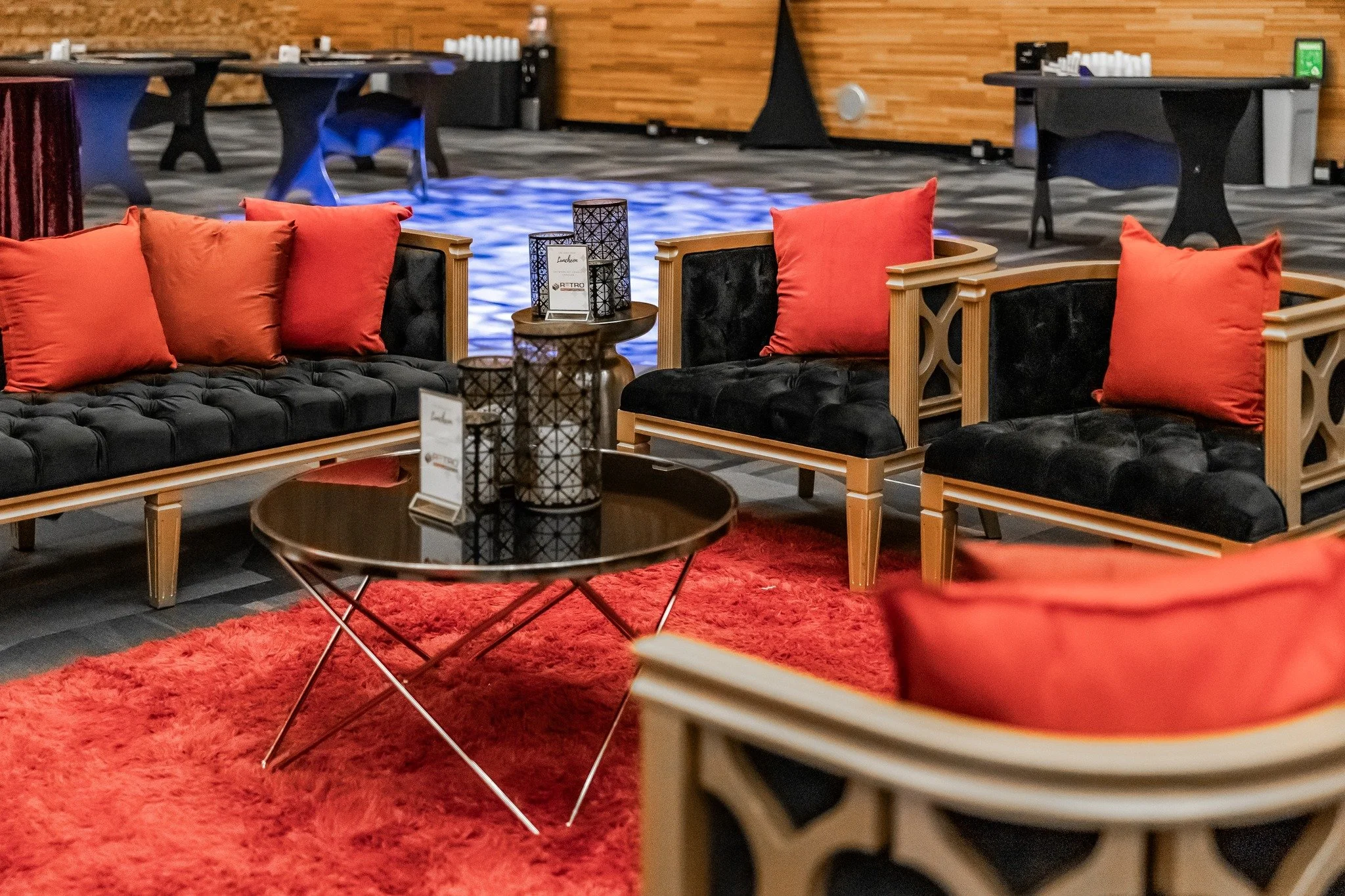 A cozy hotel lounge area with black velvet sofas, red pillows, a red shag rug, and a round black coffee table with decorative lanterns.