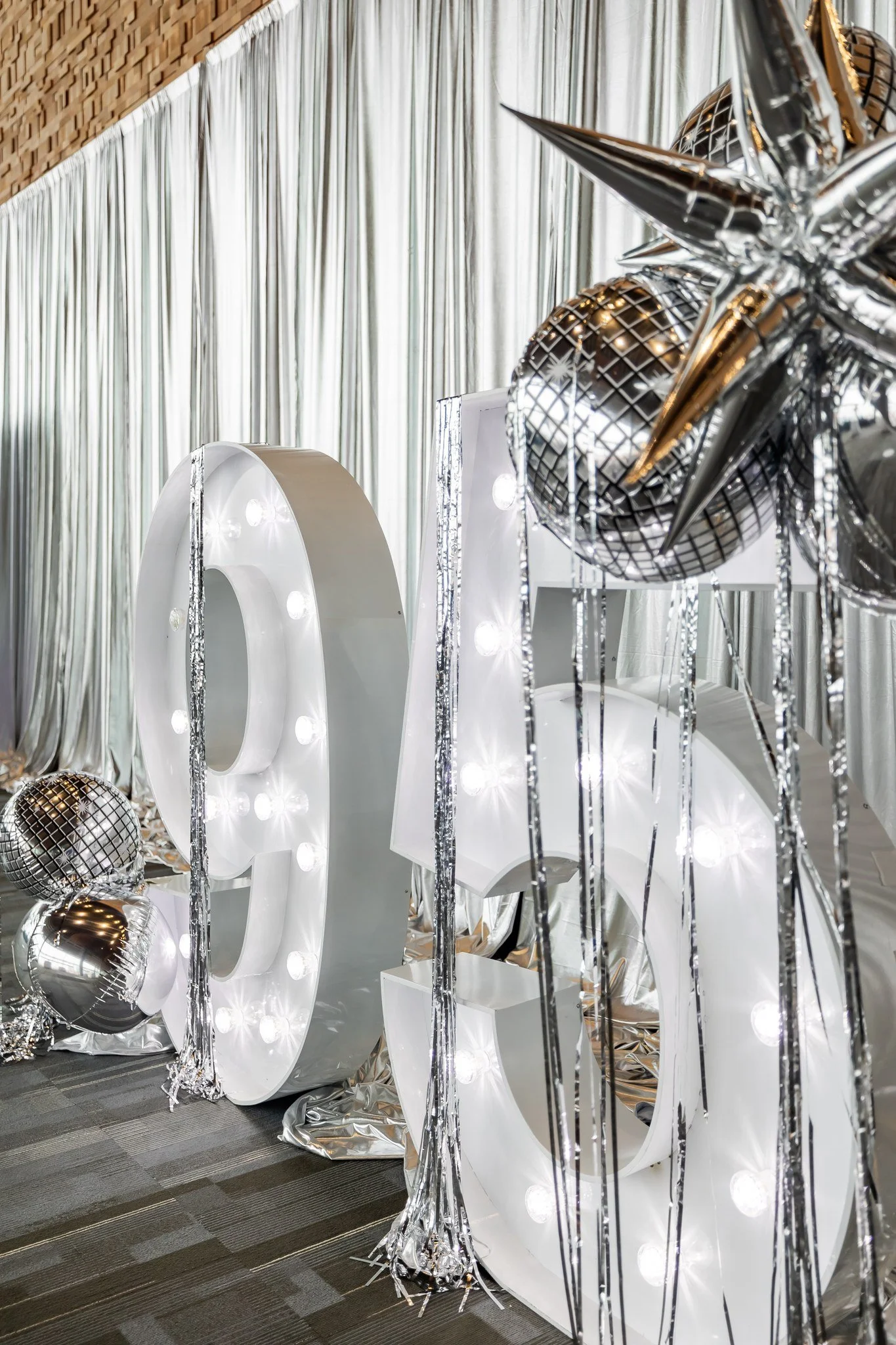 Decorative 3D numbers with lights, silver disco balls, and metallic streamers at an event