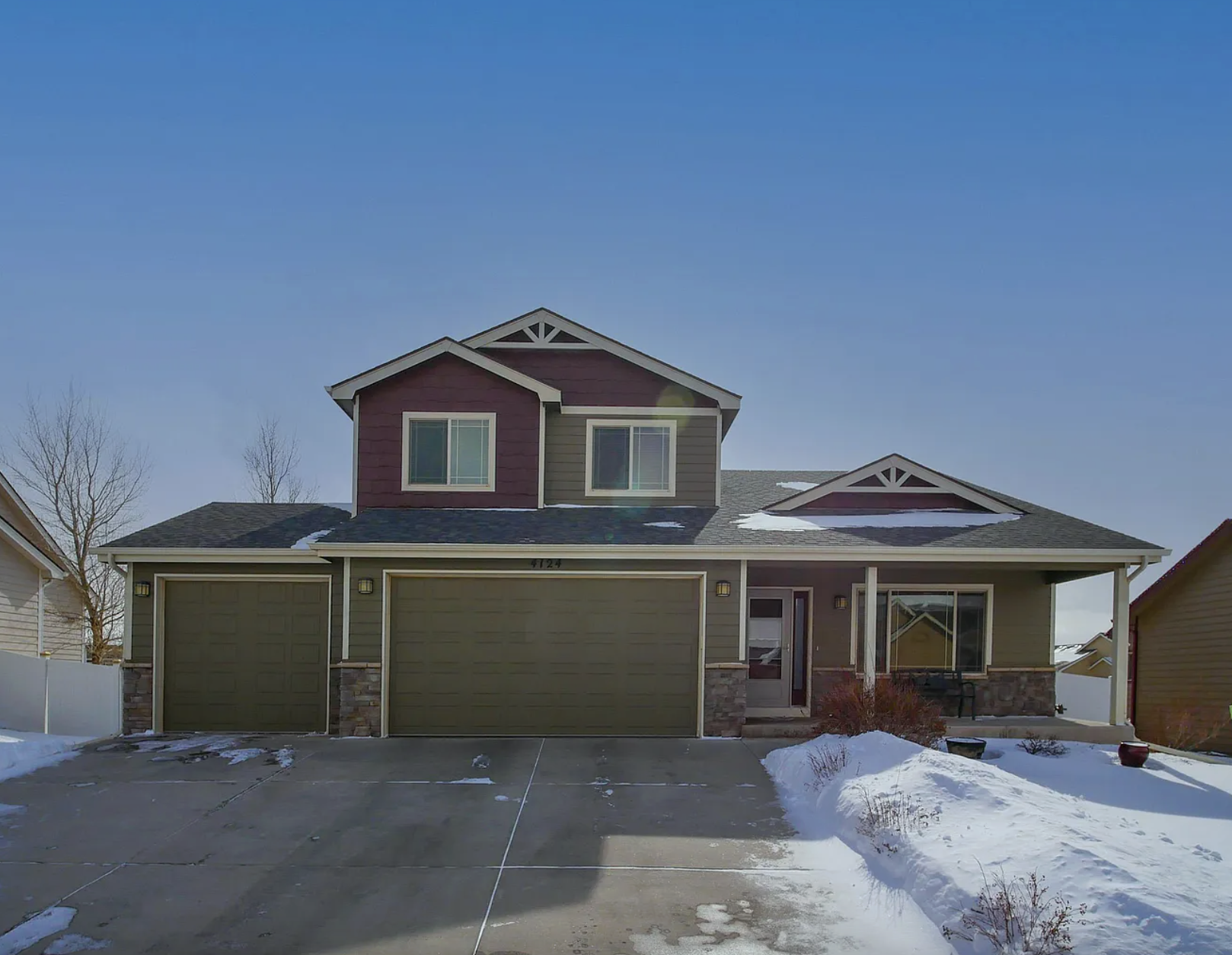 A modern two-story house with a three-car garage, stone accents, and a covered front porch, surrounded by snow and clear skies.