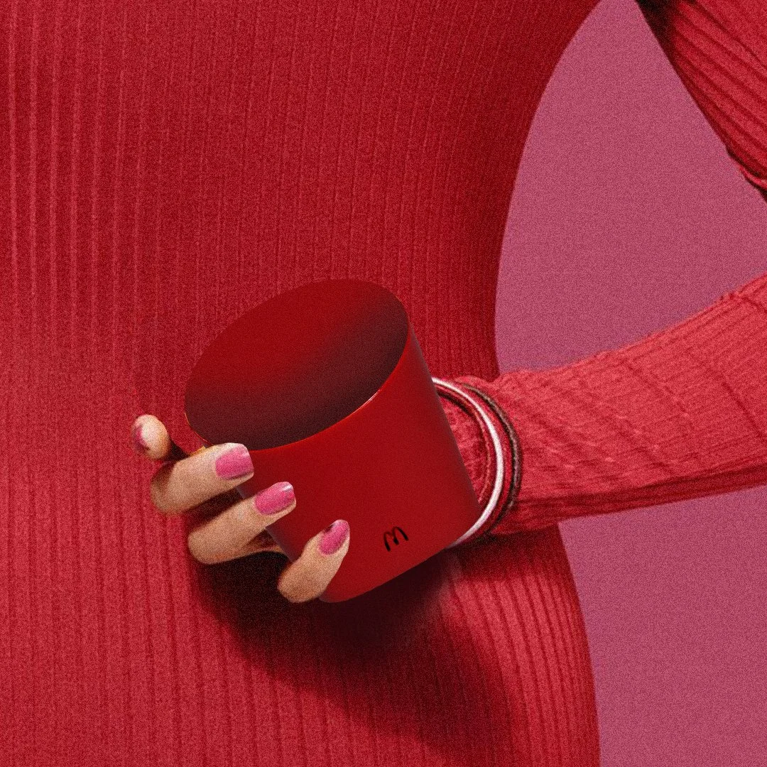 Une main tenant un grand gobelet rouge sur fond rouge, personne portant une veste ou un haut rayé rouge.