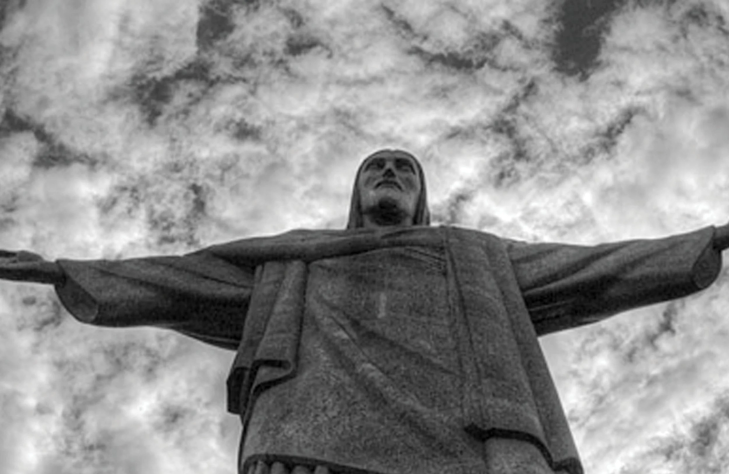Une statue du Christ avec les bras étendus, vue de dessous avec un ciel nuageux en arrière-plan.
