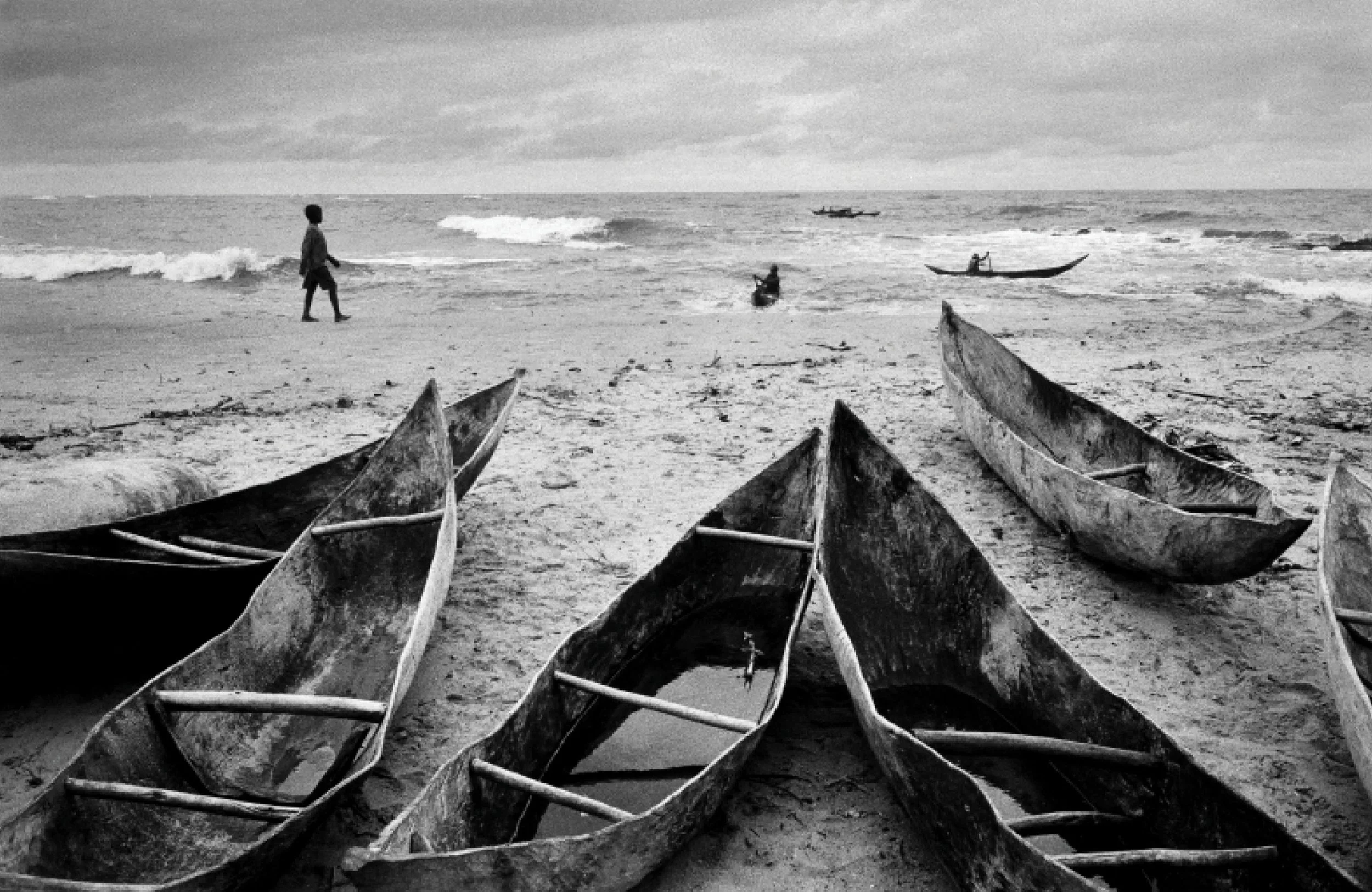 Bateaux en bois abandonnés sur la plage avec une mer agitée et un ciel nuageux en arrière-plan.