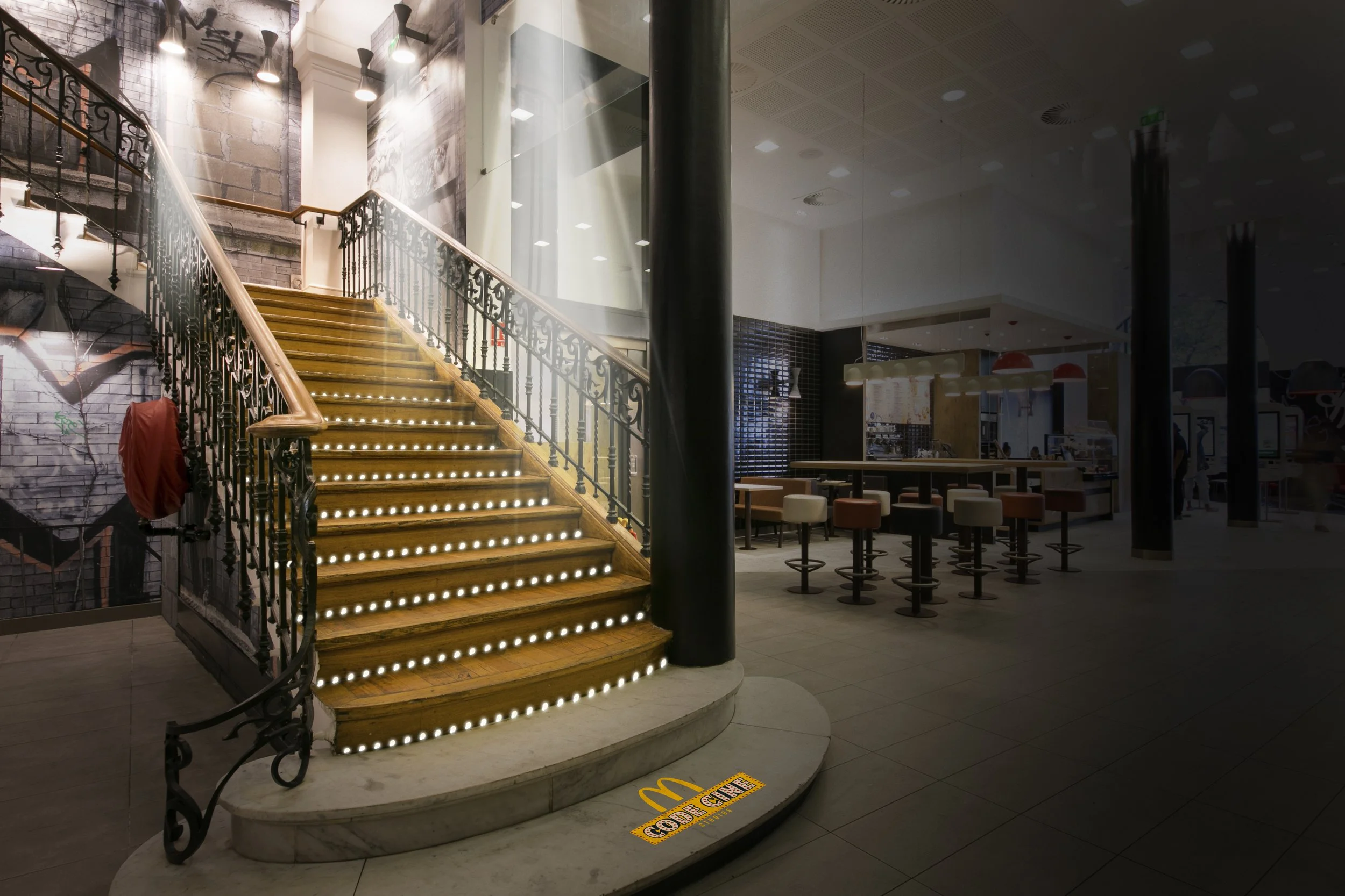 Escalier intérieur en bois avec des lumières intégrées, entouré d'une rampe en fer noir, dans un espace moderne et bien éclairé, probablement une zone de restauration ou un café.