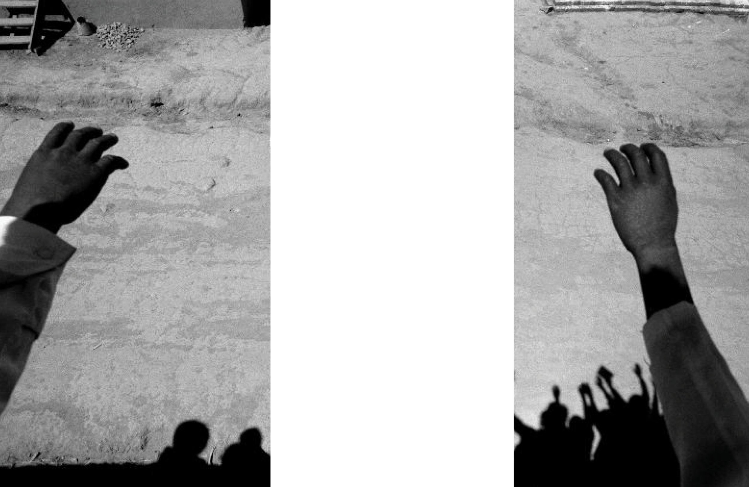 Deux mains noires, portant des costumes, se tiennent dans un environnement extérieur poussiéreux. La photo est en noir et blanc.
