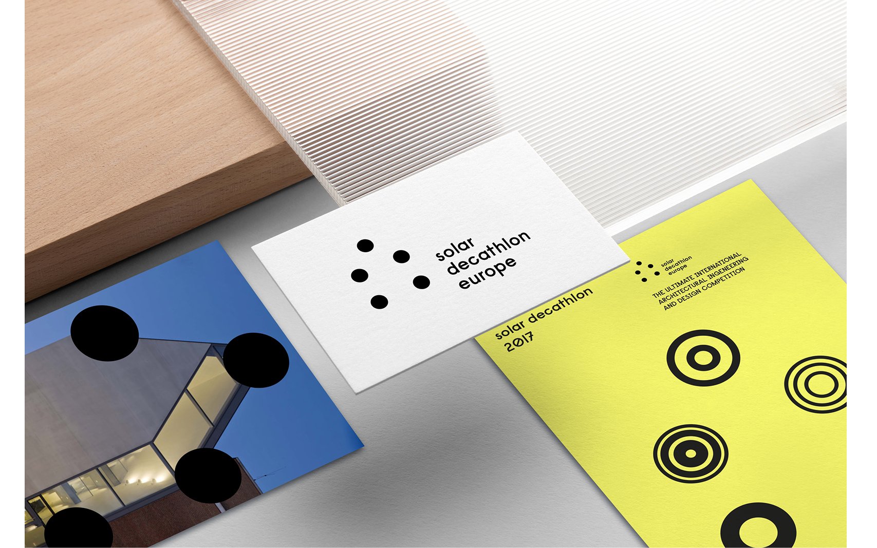 Flyers et cartes de visite pour l'événement "Solar Decathlon Europe 2017" avec logos, texte et motifs graphiques, placés sur une surface en arrière-plan.