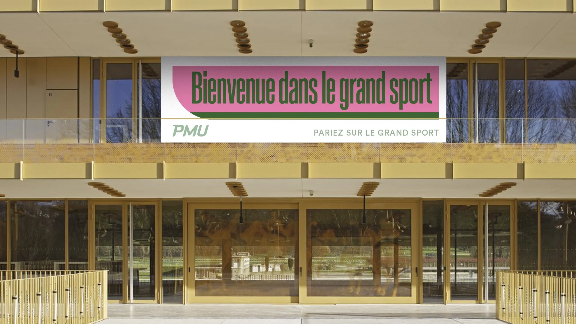 Panneau d'accueil dans un centre sportif avec le texte "Bienvenue dans le grand sport" et "PARIEZ SUR LE GRAND SPORT", bâtiment moderne avec grandes fenêtres et décoration en bois.