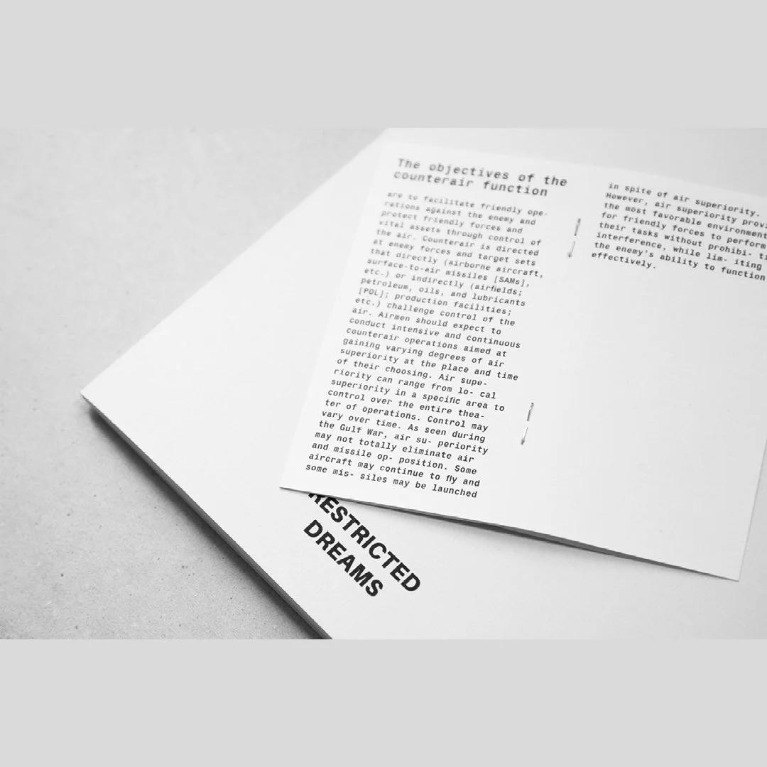 Une feuille de papier posée sur un livre ou un document avec le titre partiel 'RESTRICTED DREAMS' visible en bas à gauche.