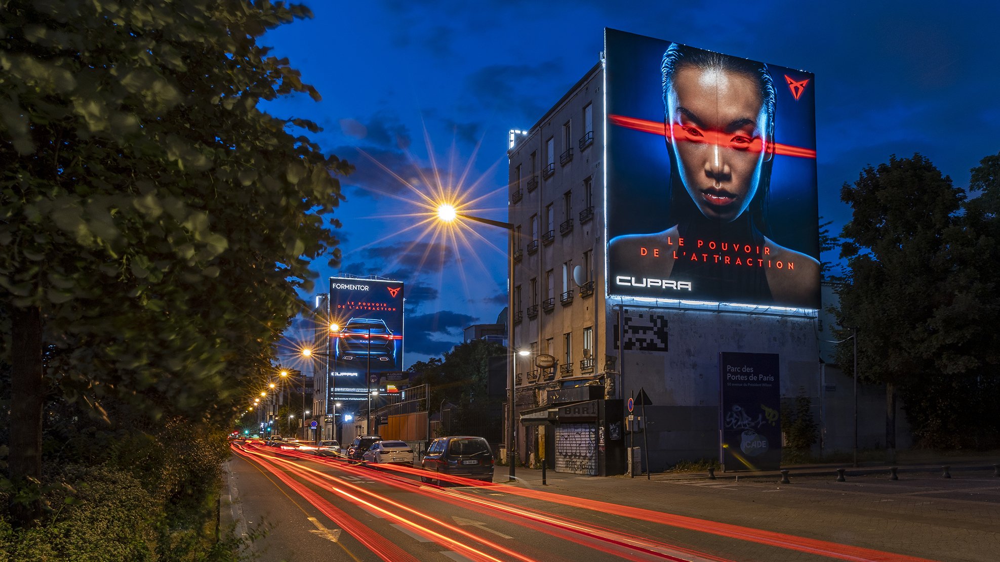 Publicité lumineuse sur un bâtiment montrant une femme avec un laser rouge traversant ses yeux, avec un texte en français "Le pouvoir de l'attraction" à Paris.
