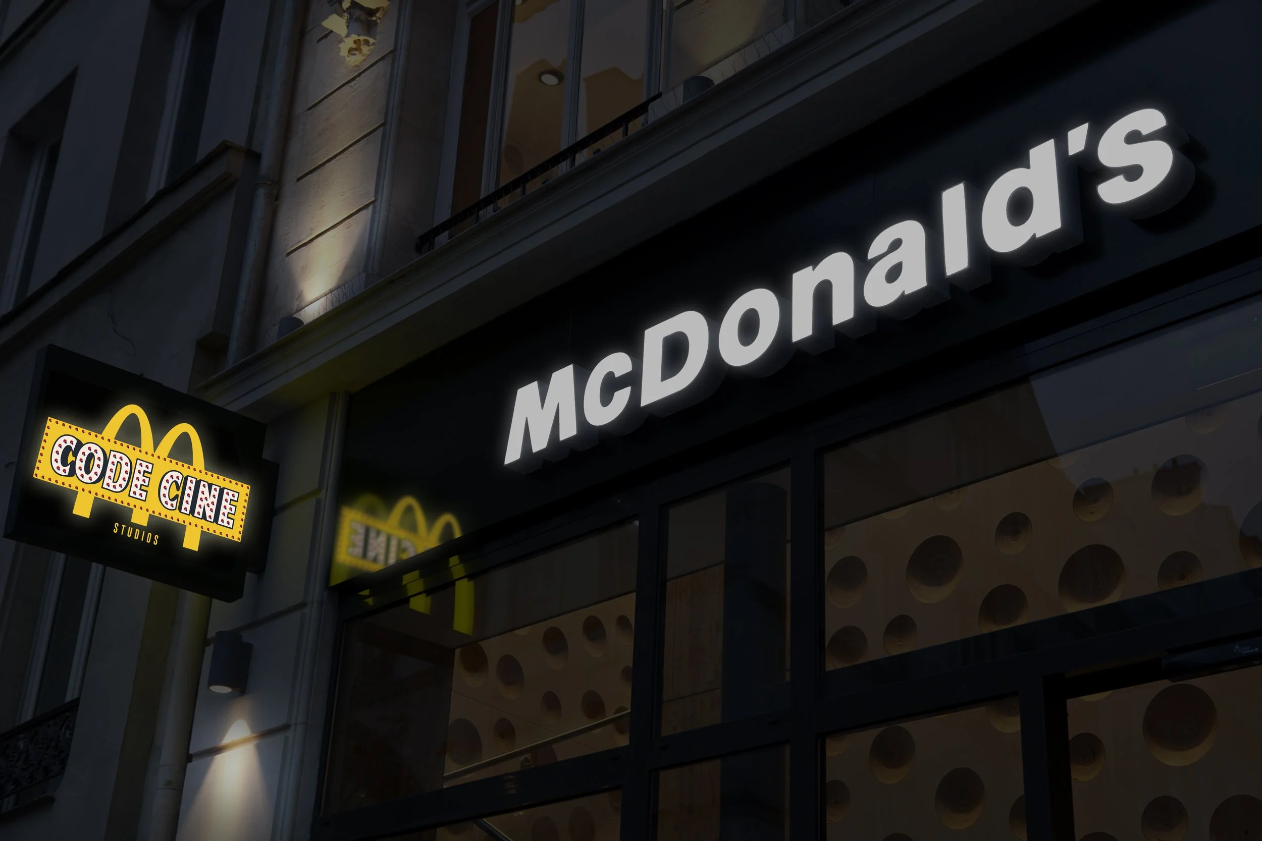 Une façade d'un bâtiment avec un panneau lumineux affichant 'McDonald's' en lettres blanches lumineuses. Il y a également un autre panneau noir avec des lettres jaunes indiquant 'CODE GINE STUDIOS'.