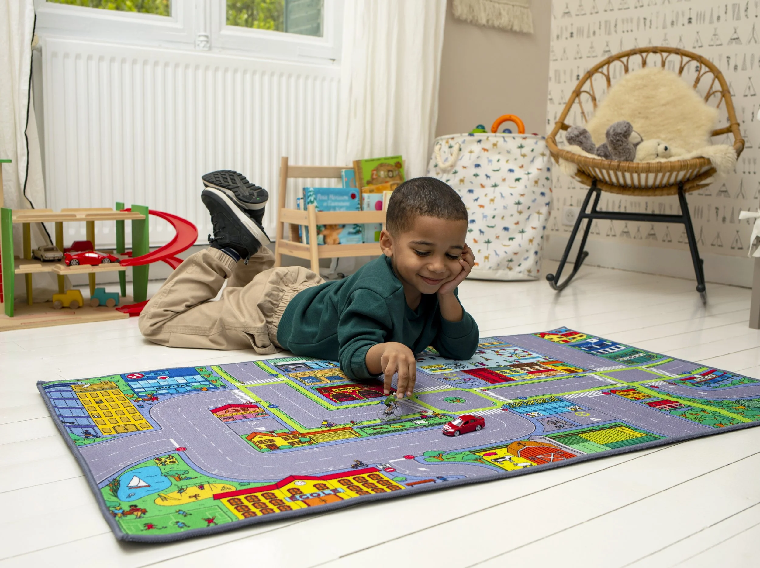 Un jeune garçon joue avec des voitures sur un tapis de jeu représentant une ville à l'intérieur d'une pièce lumineuse.