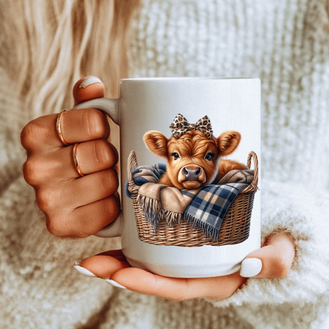 Female holding Cute Highland Cow Basket Mug unique coffee mug, highlighting the baby cow in basket with blanket design, from Coffee and Moo.