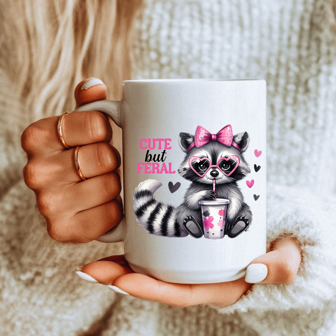 Female holding Cute But Feral Raccoon unique coffee mug, highlighting the "Cute but feral" design, from Coffee and Moo.