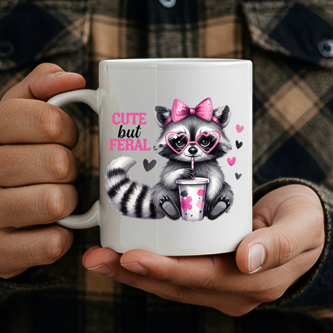 Male holding Cute But Feral Raccoon humorous coffee mug, showcasing the design and comfortable grip, by Coffee and Moo.