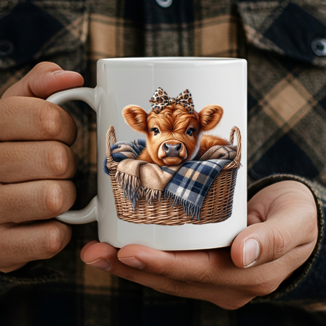 Adult holding Cute Highland Cow Basket Mug humorous coffee mug, showcasing the baby cow in basket design, by Coffee and Moo.