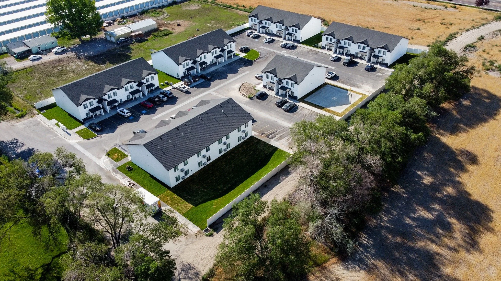 Aerial view of a residential apartment complex with multiple white buildings, parking lots, green lawns, and trees.