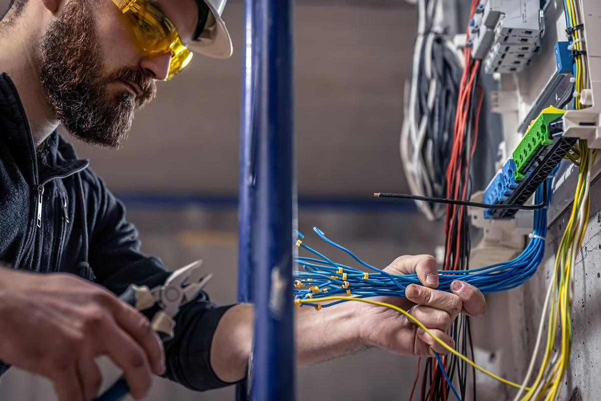 A male technician working on electrical wiring inside an electrical panel or circuit board.