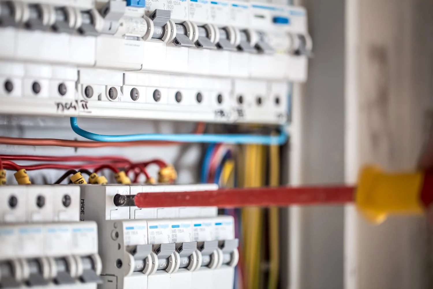 Close-up of an electrical panel with circuit breakers, colored wires, and electrical connections.