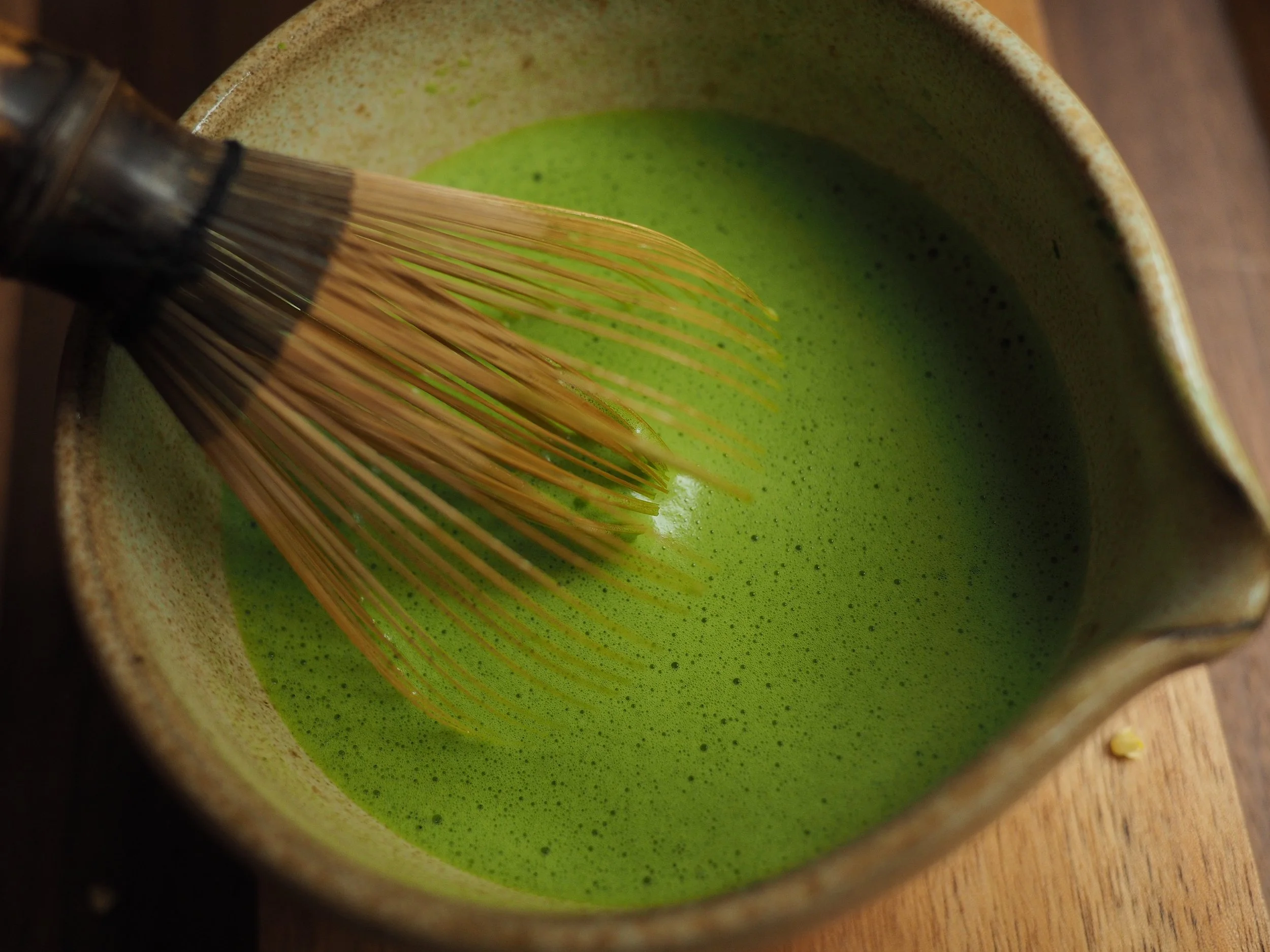 A close up photograph of a matcha whisk in a bowl of frothy, vivid green matcha