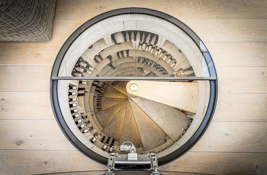 A spiral staircase viewed from above, with wine bottles stored on the sides and a wooden floor surrounding it.