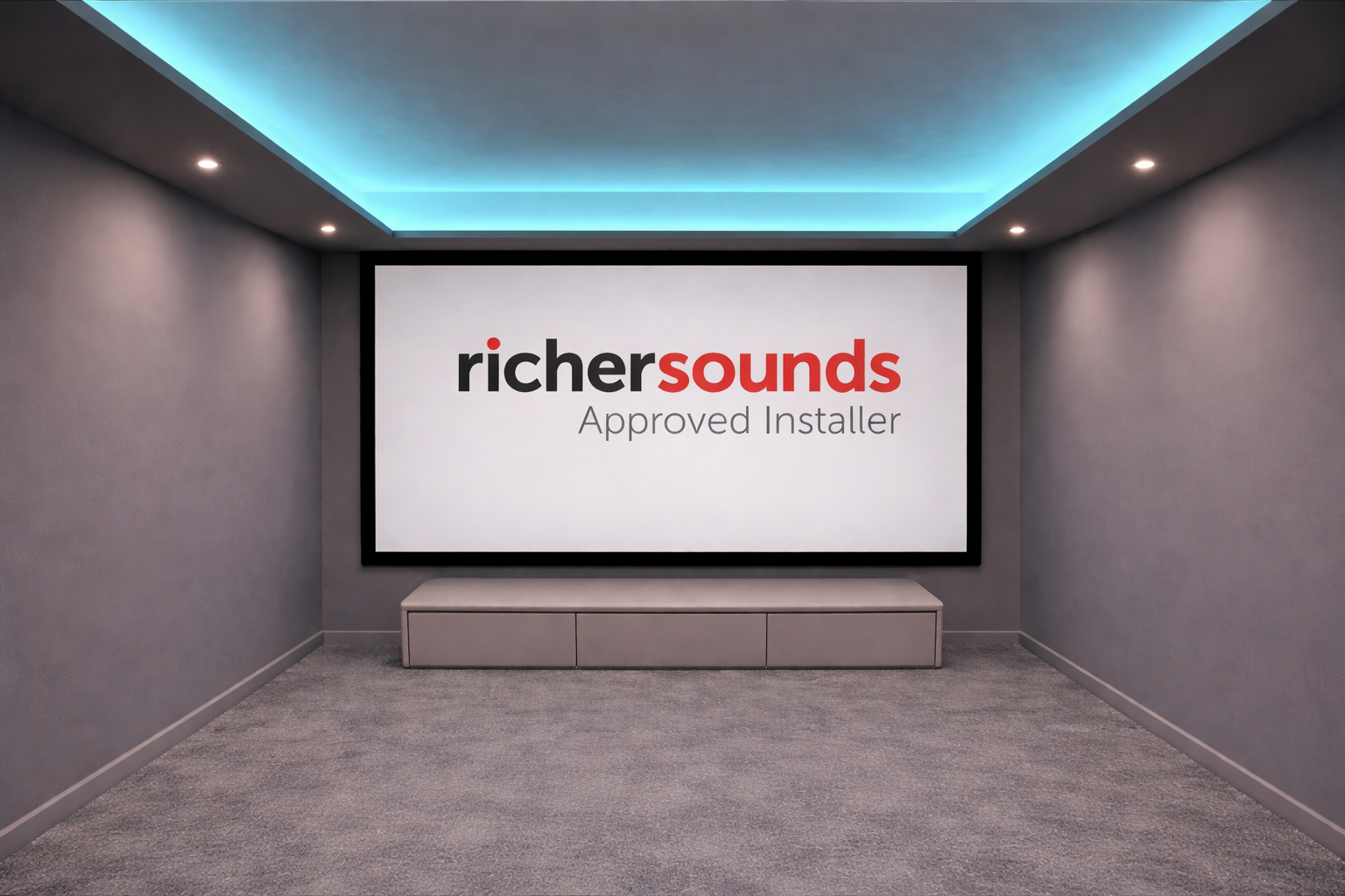 A home theater room with a large screen displaying the logo 'richersounds Approved Installer' and a gray cabinet at the bottom. The room has gray walls, a gray carpet, and ceiling with blue ambient lighting and recessed lights.