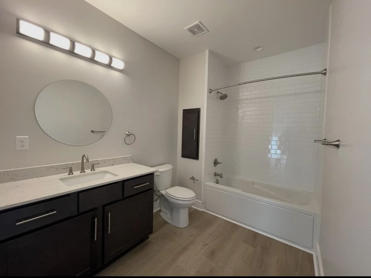 Modern bathroom with a vanity, mirror, toilet, and bathtub with sliding glass doors and a white subway tile wall at the shower area.