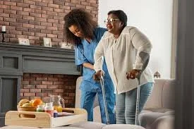 Two women enjoying a moment together in a cozy living room, one wearing a white sweater and glasses, the other in a blue outfit, near a fireplace with a tray of food on a table.