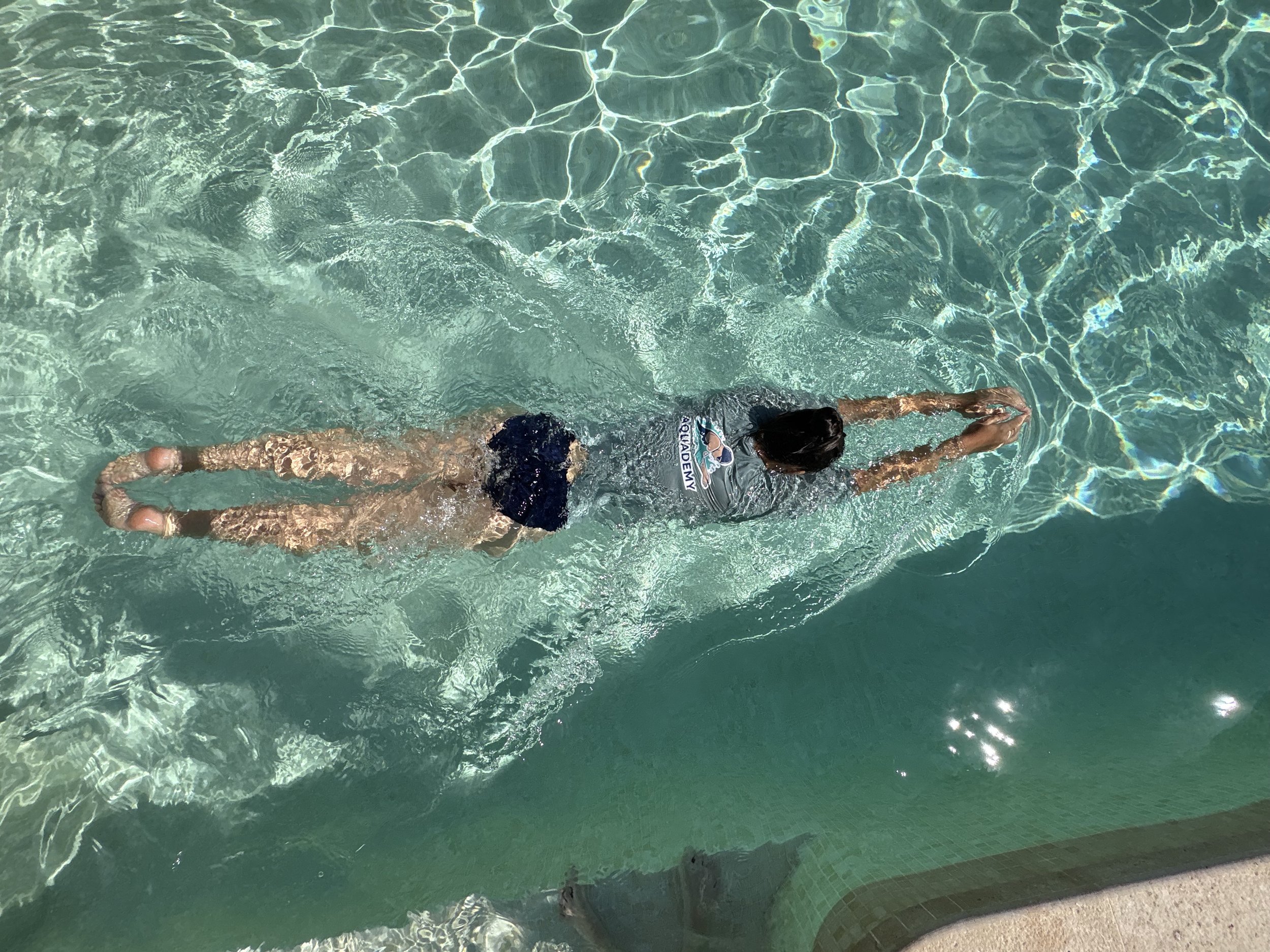 Une personne nage dans une piscine claire avec les bras tendus devant elle et la tête immergée dans l'eau.
