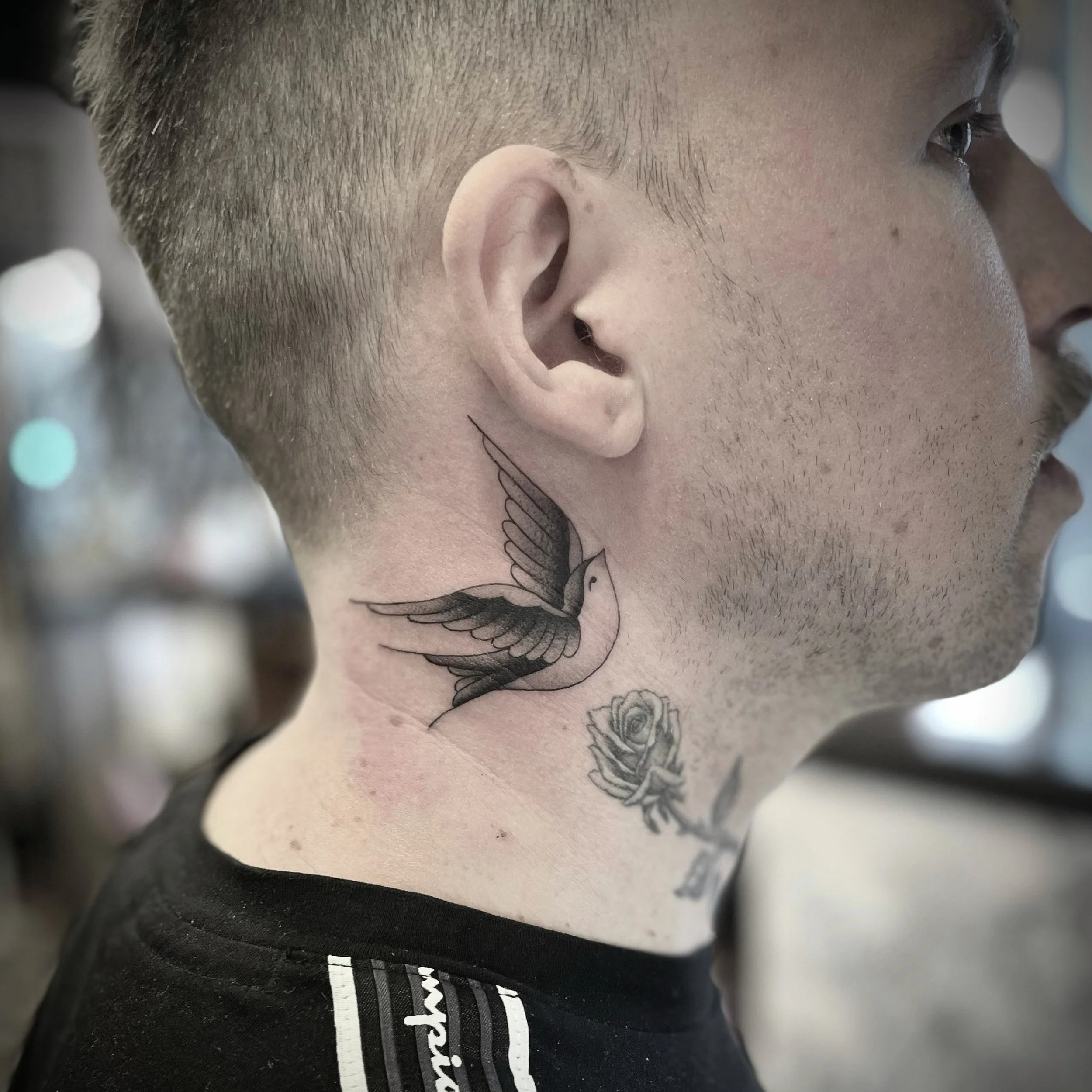 A close-up of a man's neck and face, revealing a tattoo of a flying bird and a flower on his neck.