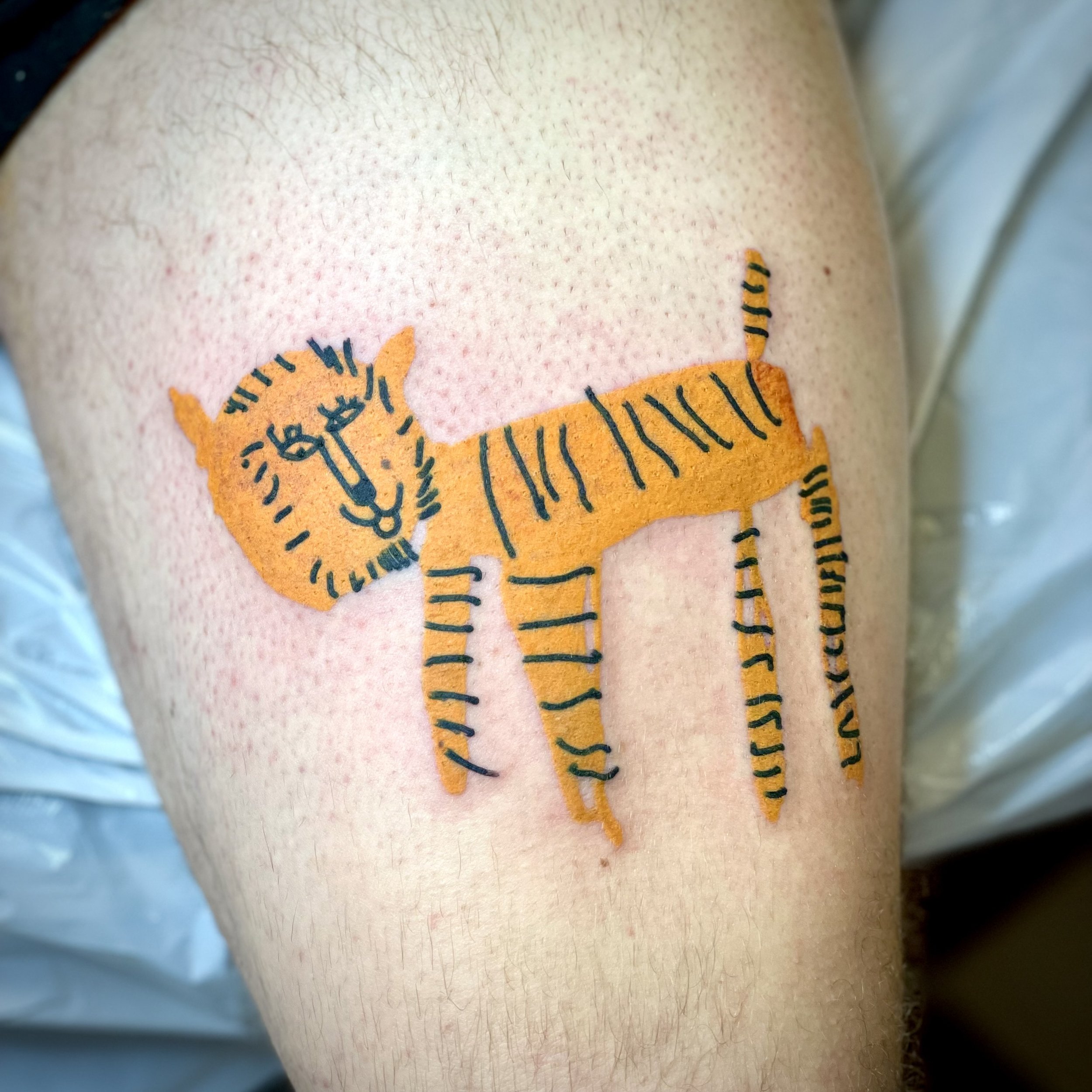 Temporary tattoo of a tiger with a clock face on its head, and black stripes on an orange background, on someone's upper arm.