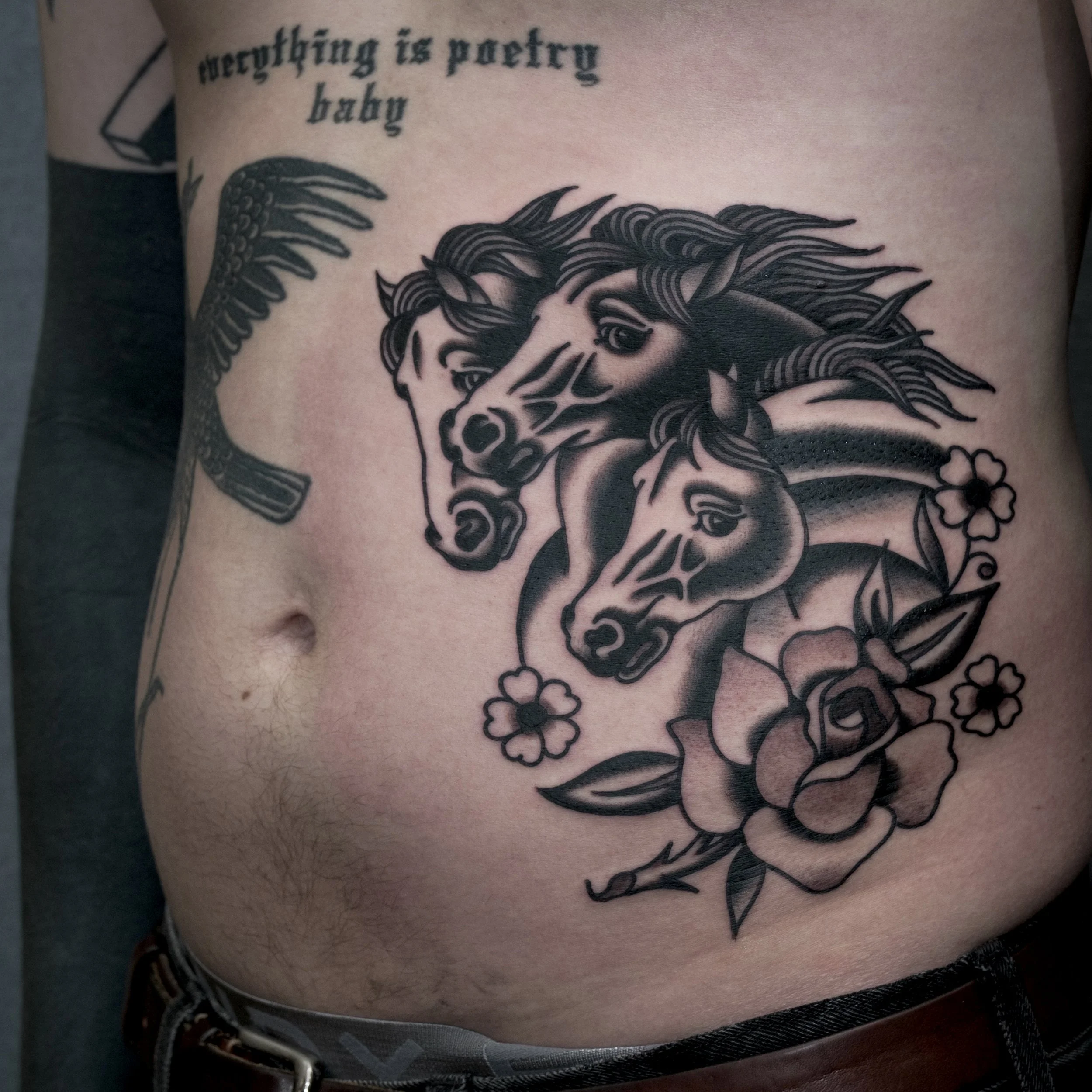 Tattoo of two horses' heads with flowing manes, surrounded by flowers, on a person's side.