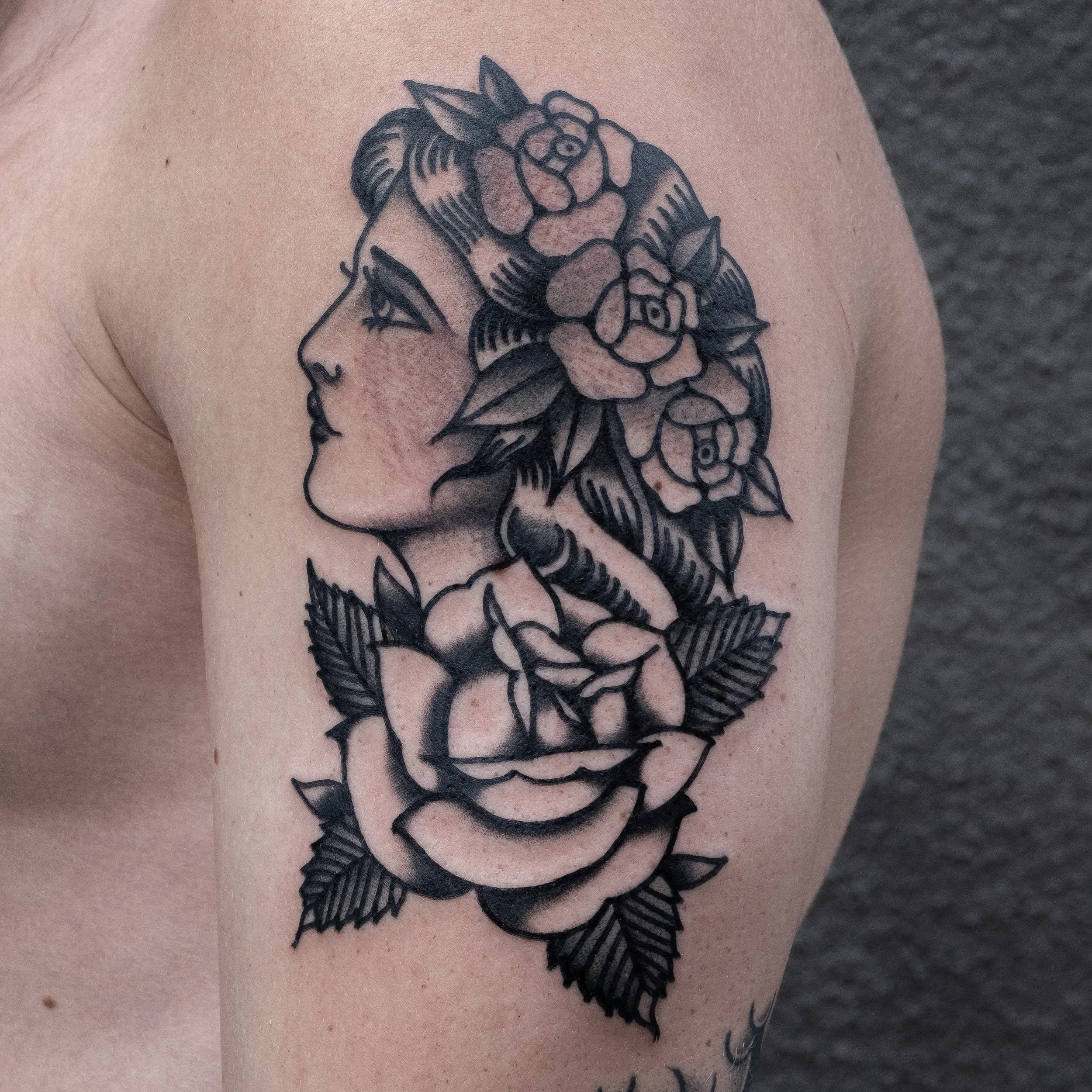 Tattoo of a woman's profile with flowers and leaves on her head and around her neck.