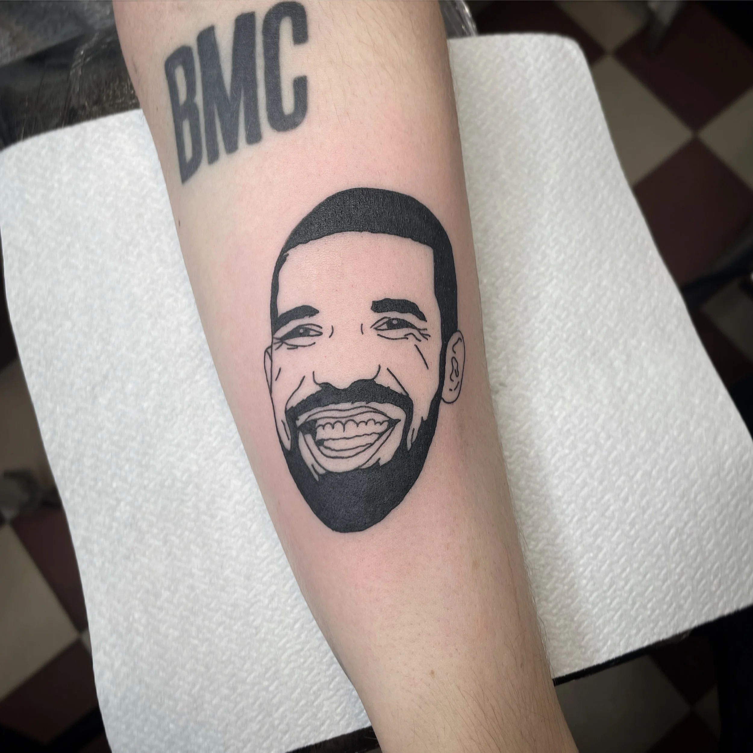 Tattoo of a smiling man's face with a beard and the word 'BMG' above it.