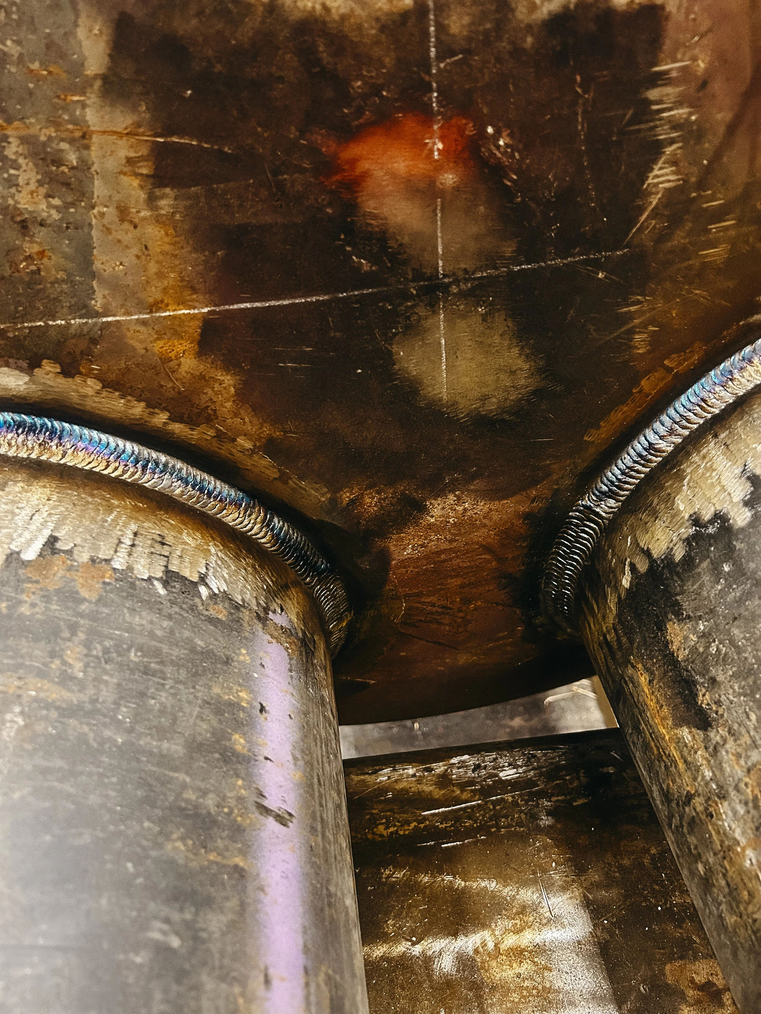 Close-up view of two welded metal pipes connected underneath a rusty metal surface.