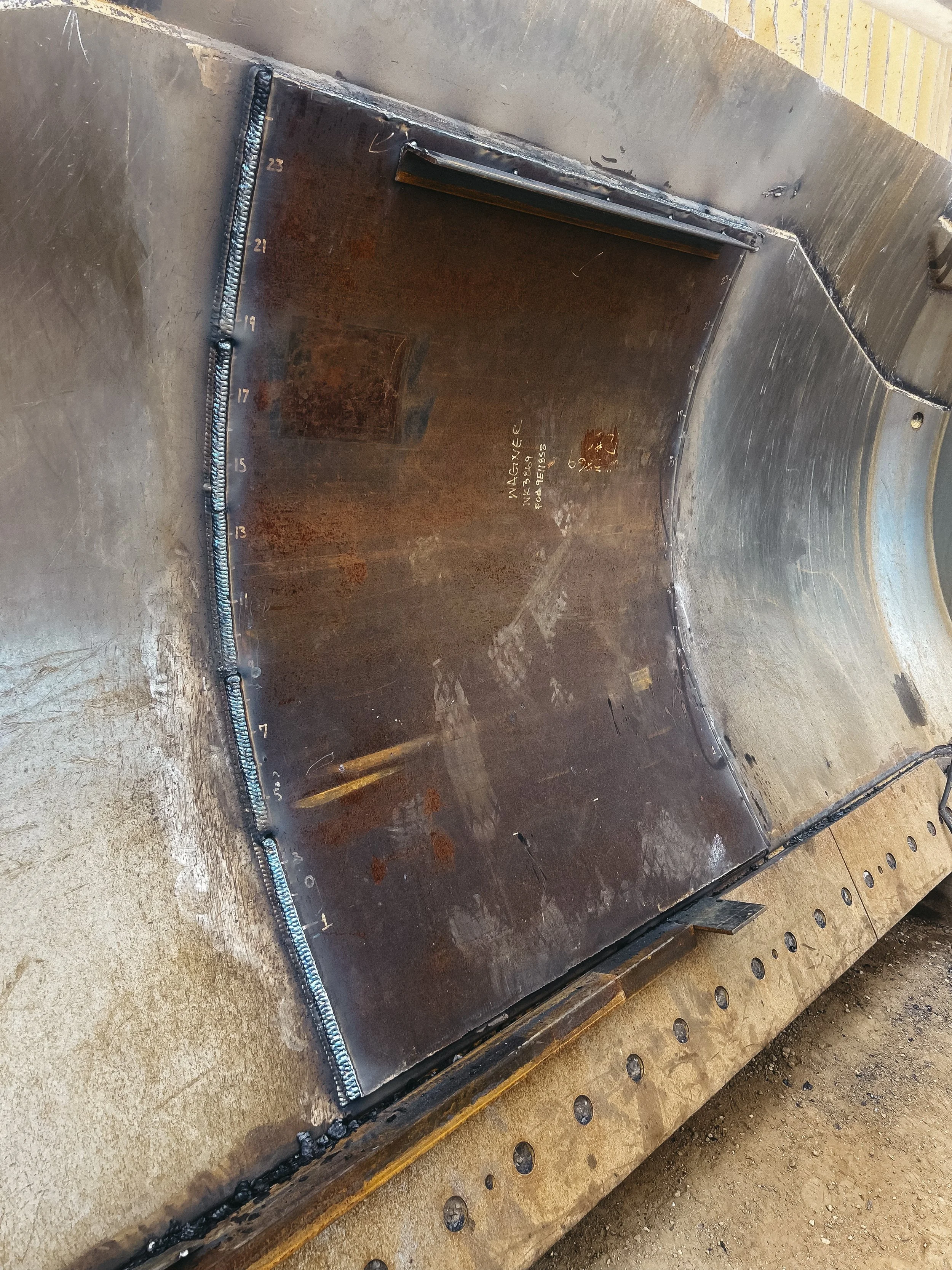 Close-up of a metal welding project with a curved seam and measurements marked along the edge, on a metallic surface.