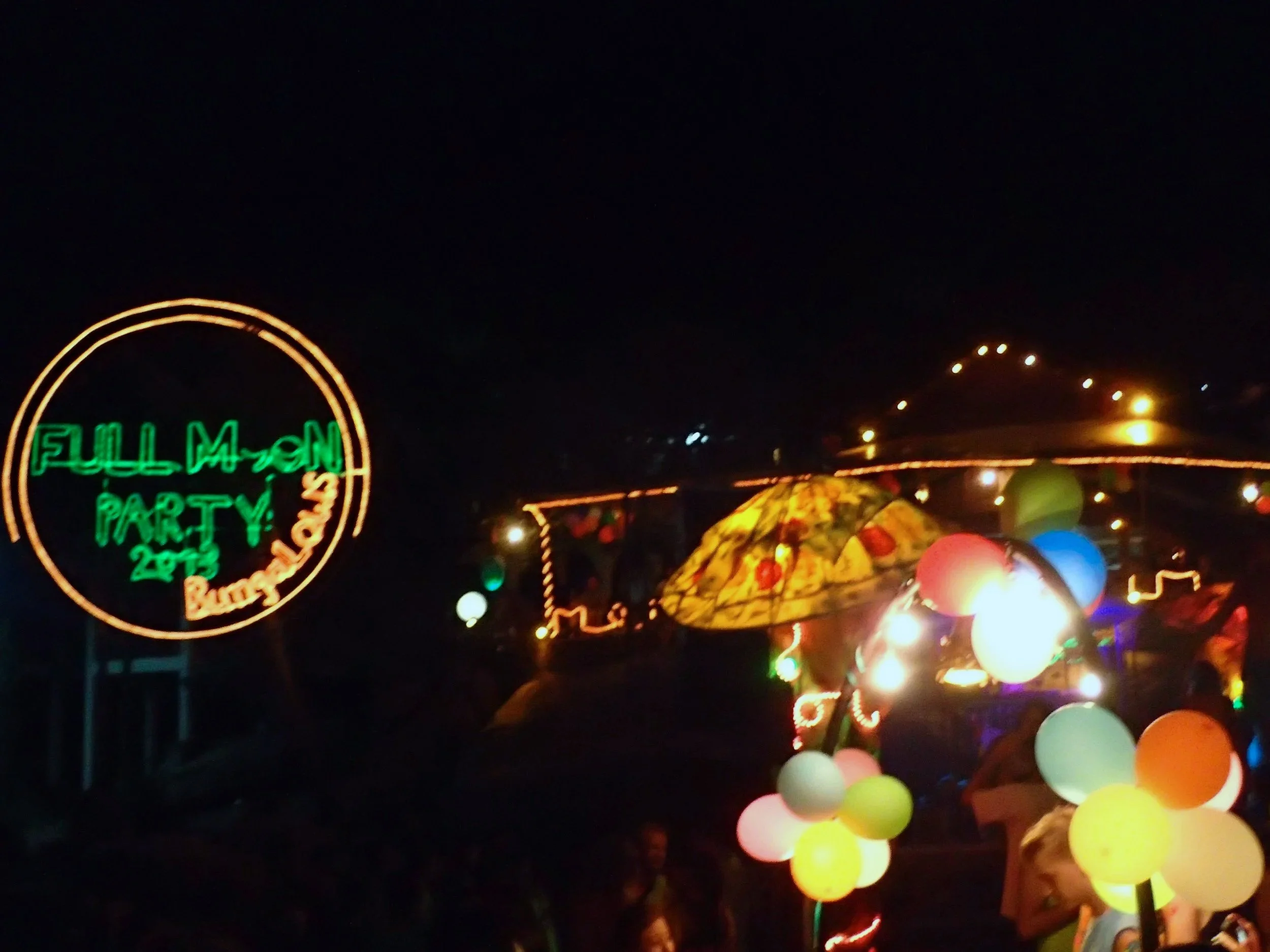 Night scene of a theme park with colorful balloons, neon lights, and a sign that reads 'FULL MOON PARTY 22.'