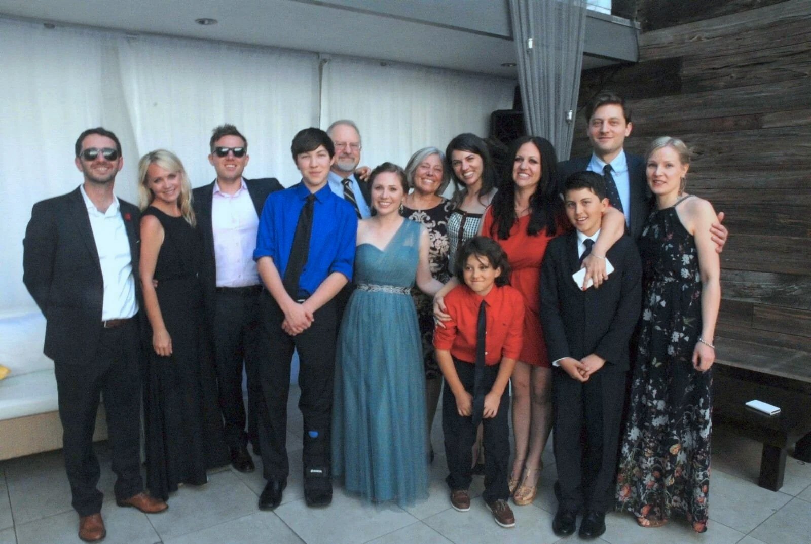 A group of fifteen people dressed in formal attire posing for a photo at an indoor event or celebration.