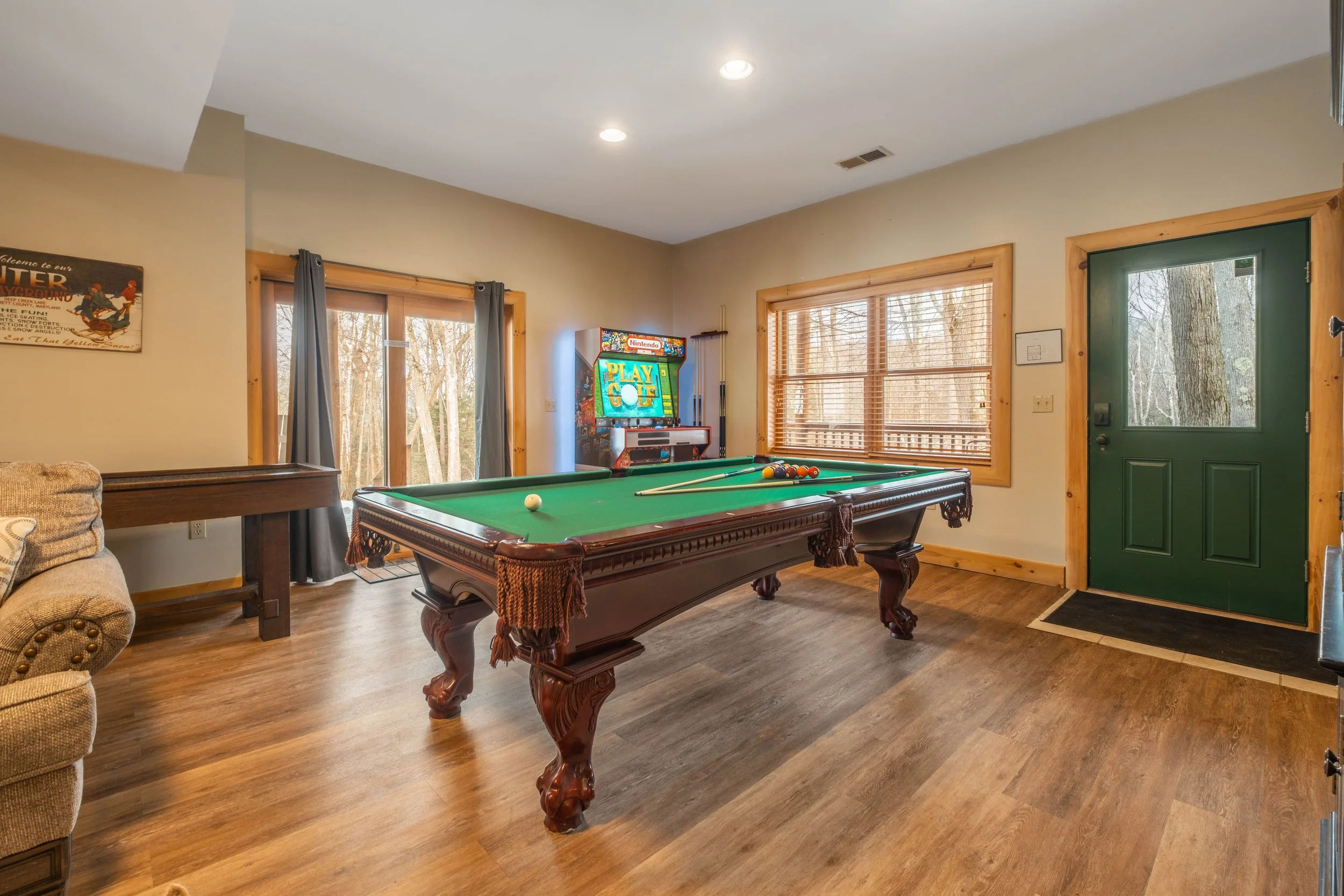 Living room with pool table, wooden floors, green front door, window blinds, and a TV with a Nintendo Play Golf game on screen.