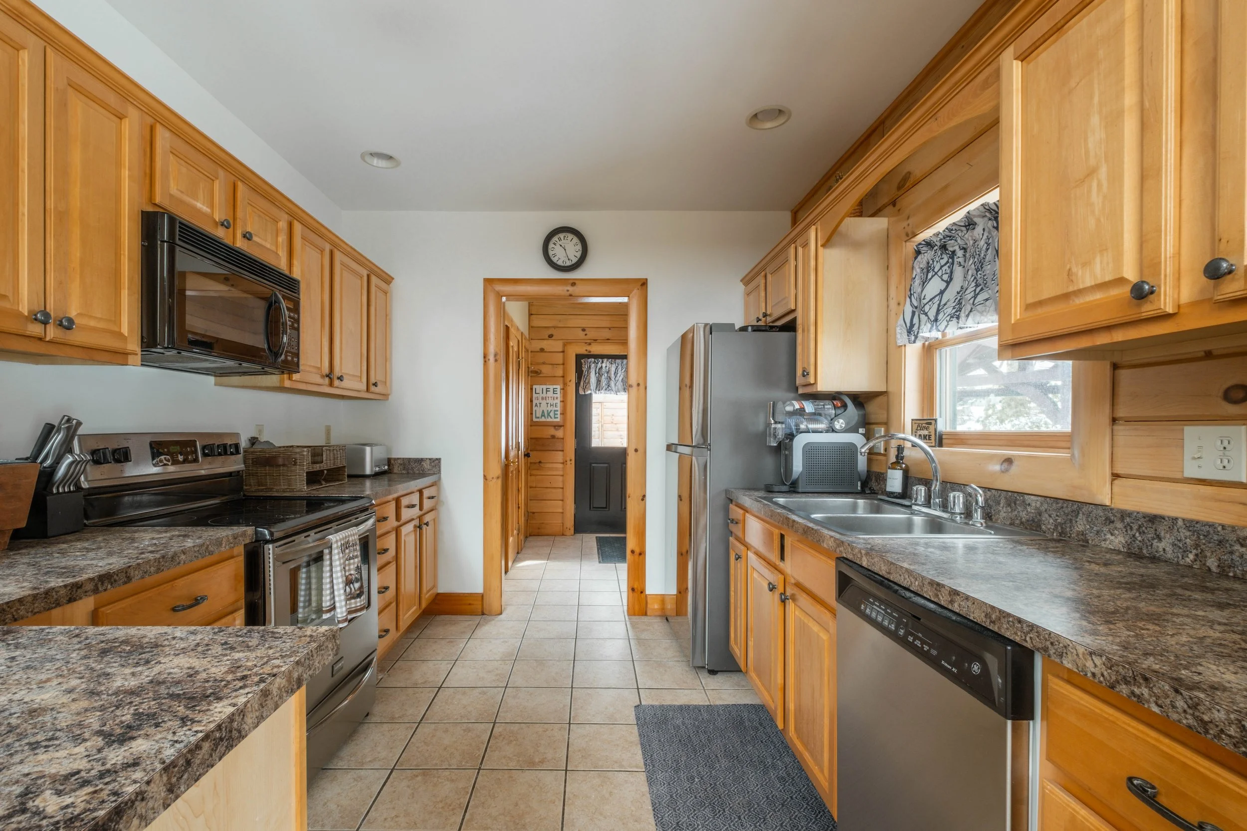 Kitchen with wooden cabinets, granite countertops, stainless steel appliances, a window above the sink, and a clock on the wall.