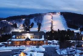 Snow-covered mountain at night with ski slopes illuminated by lights, and a building at the base.