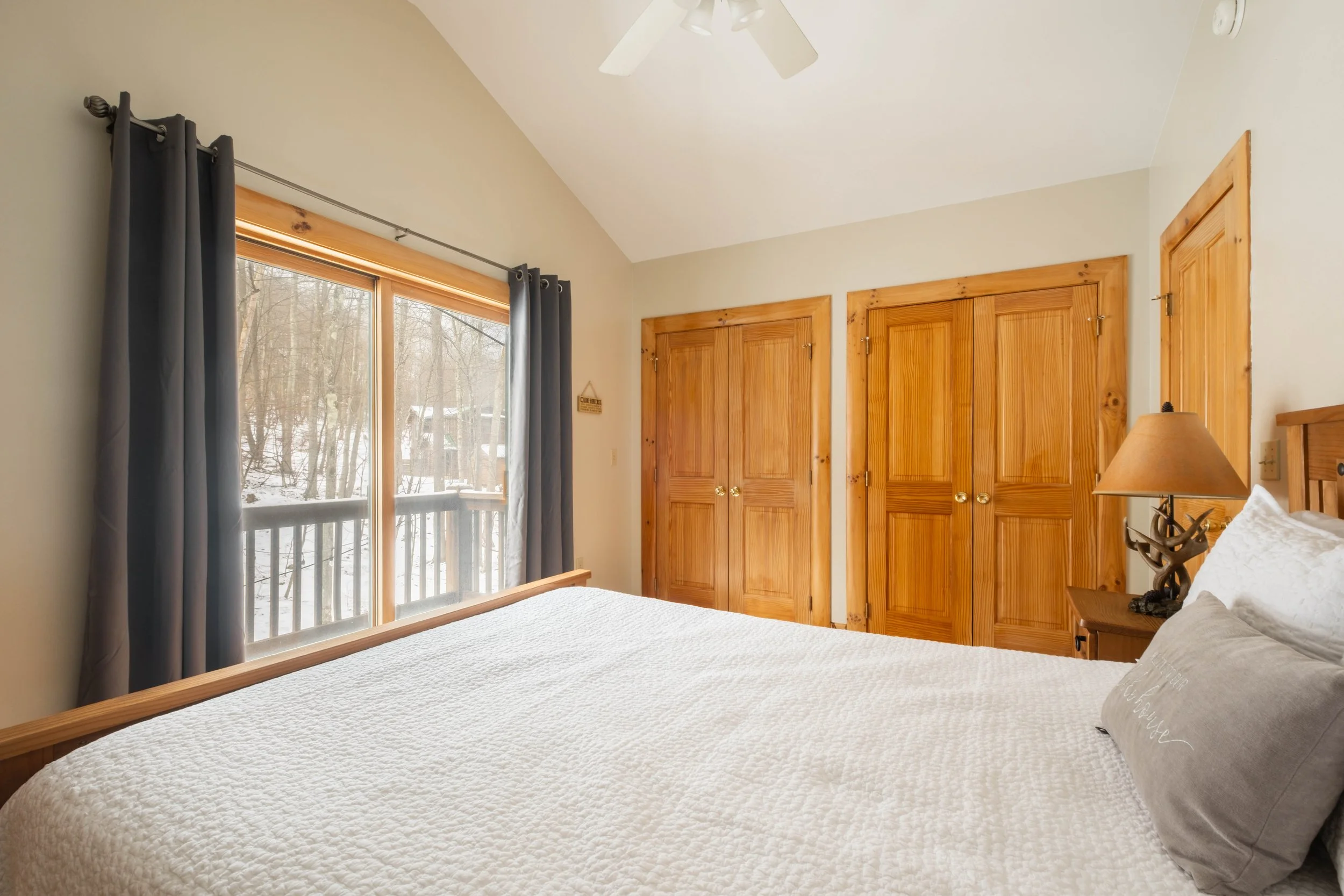 Bedroom with a large bed, wooden closets, a window with dark curtains, and a nightstand with a lamp featuring a deer antler design.